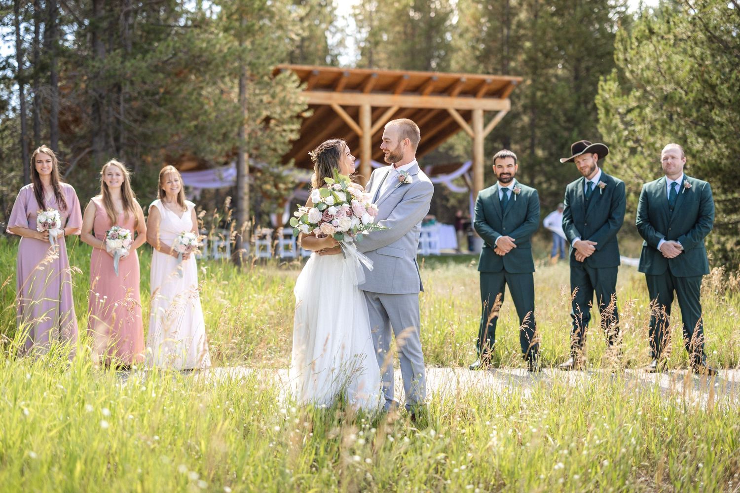 A wedding ceremony moment captured outdoors with bridal party in a meadow setting.