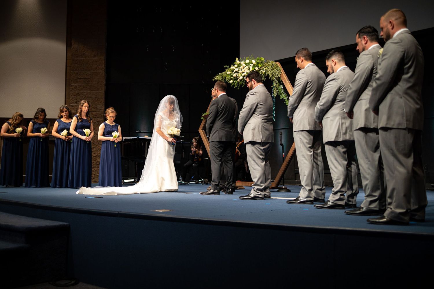 Wedding party lined up on stage during ceremony with dramatic lighting.