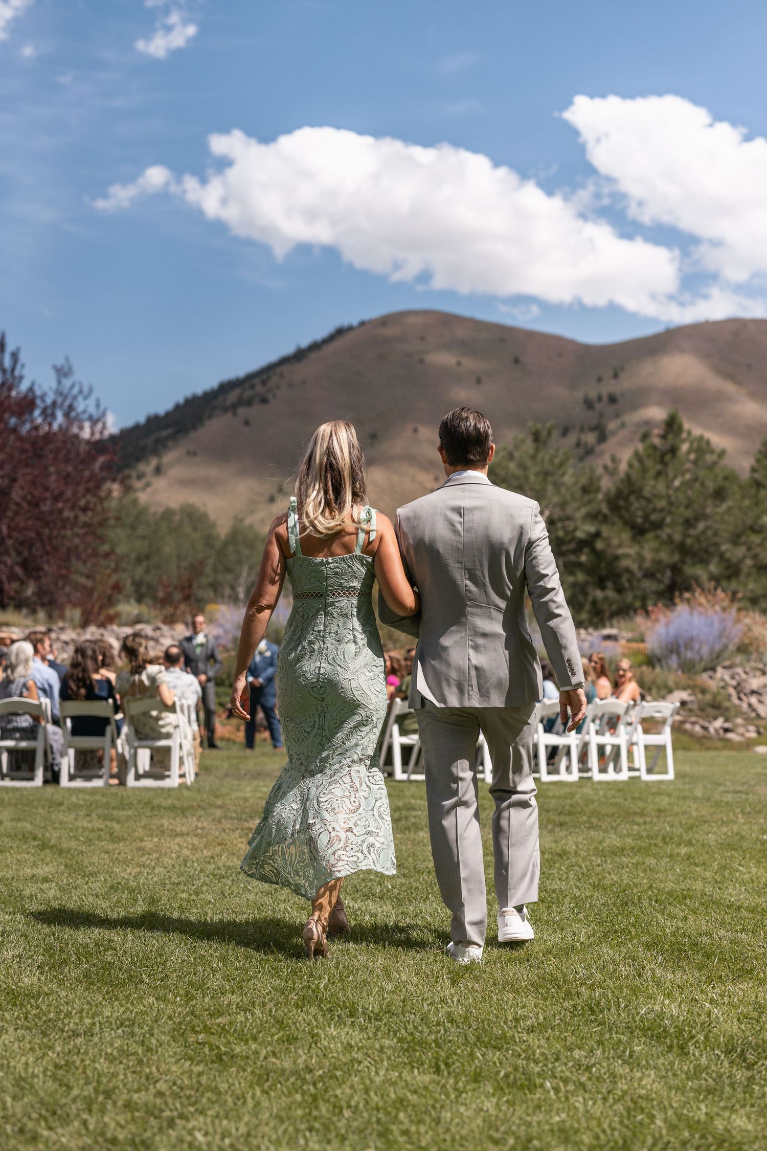 Wedding party walking across green lawn with mountain backdrop.