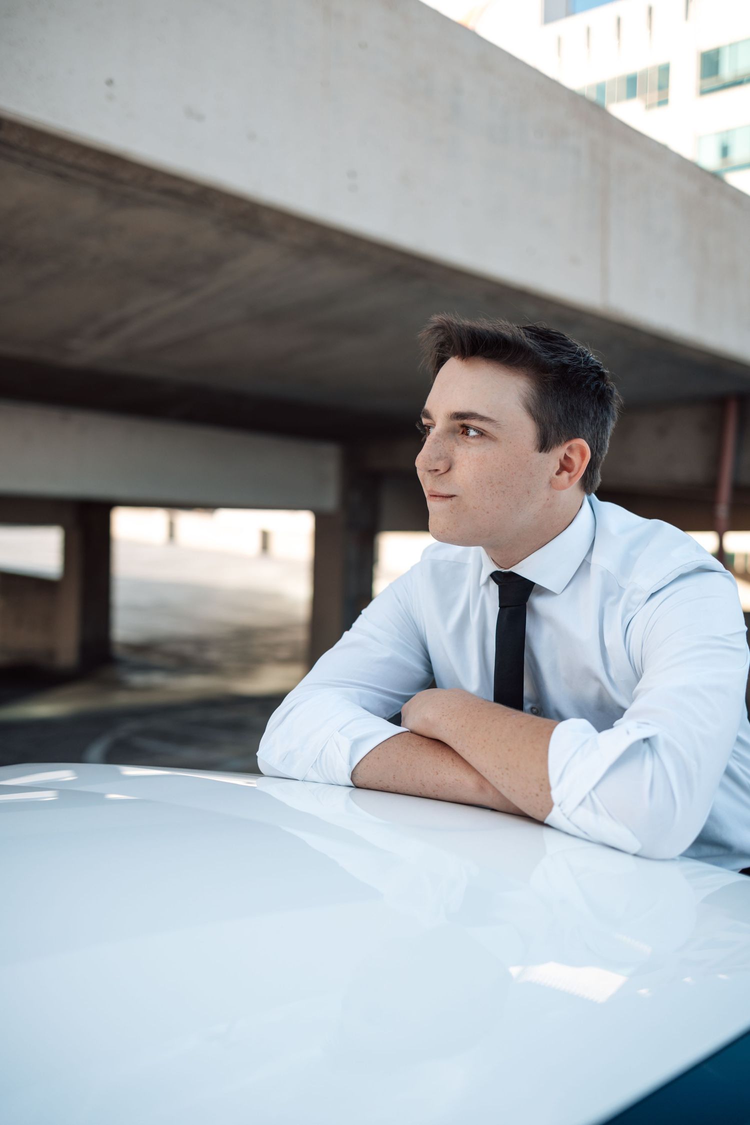 Professional in white dress shirt and tie leans thoughtfully against white surface in minimalist setting.