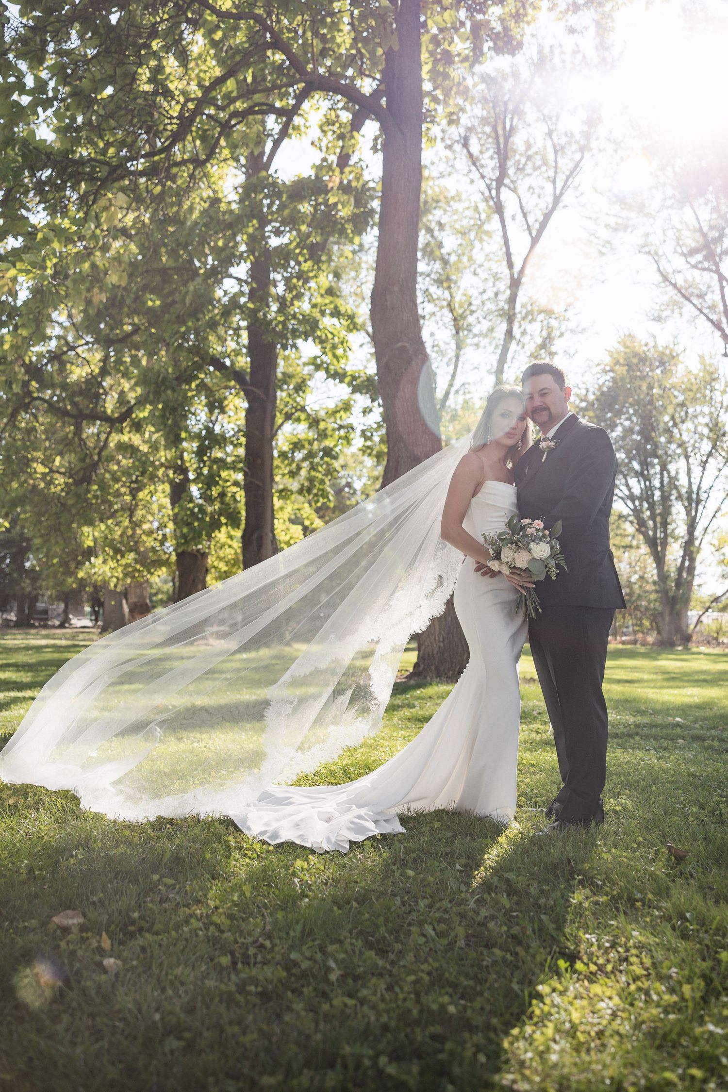 Wedding couple poses as bride's veil flows dramatically in the breeze.