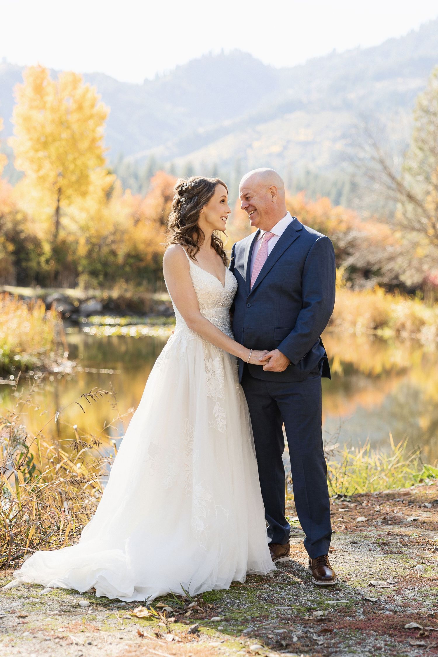 A couple shares a romantic moment by a lake with fall foliage and mountains in the background.
