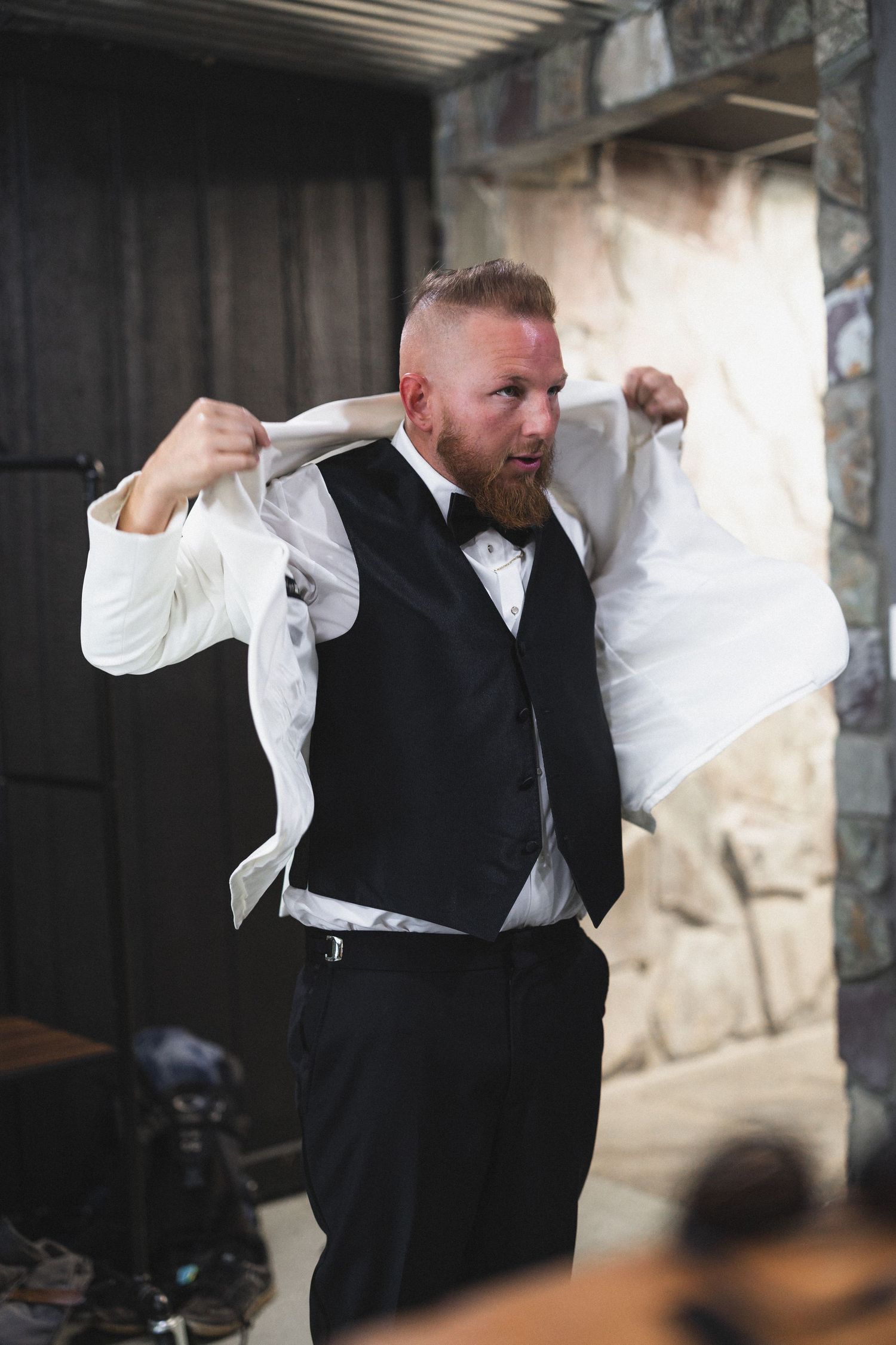 Groom putting on white formal jacket before wedding ceremony.
