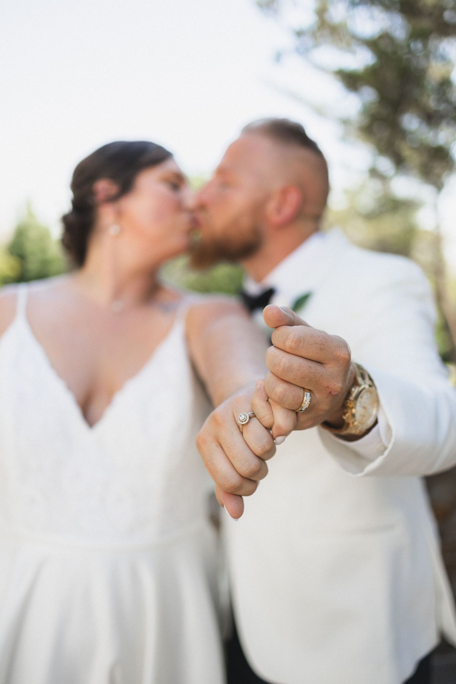 Close-up of intertwined hands with wedding rings during an outdoor ceremony.