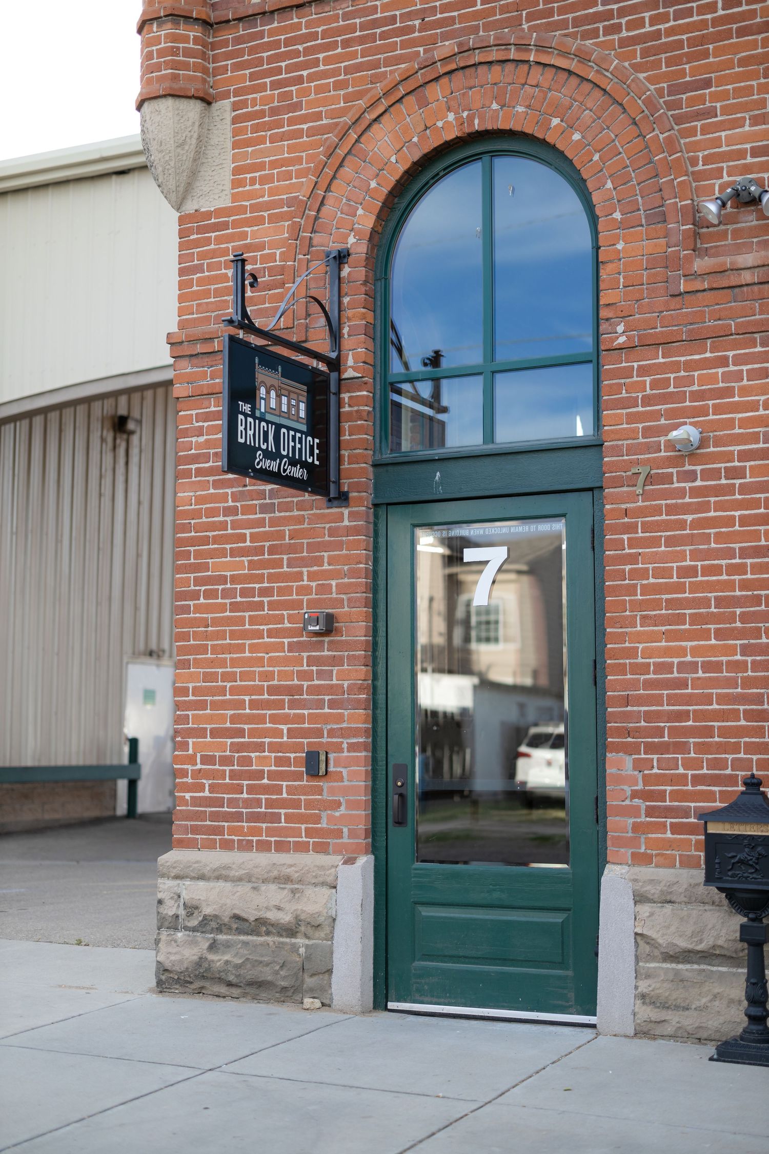 Green door entrance to brick building with arched window and hanging sign.