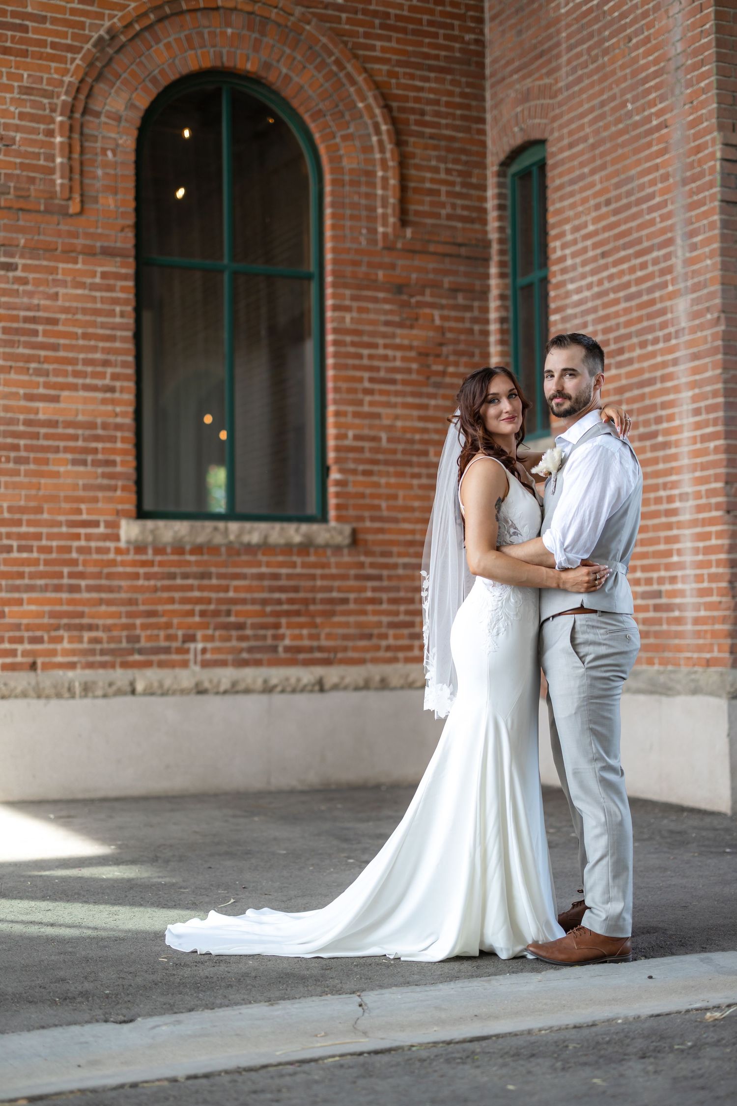Elegant bride and groom pose together in front of a red brick church with arched windows.