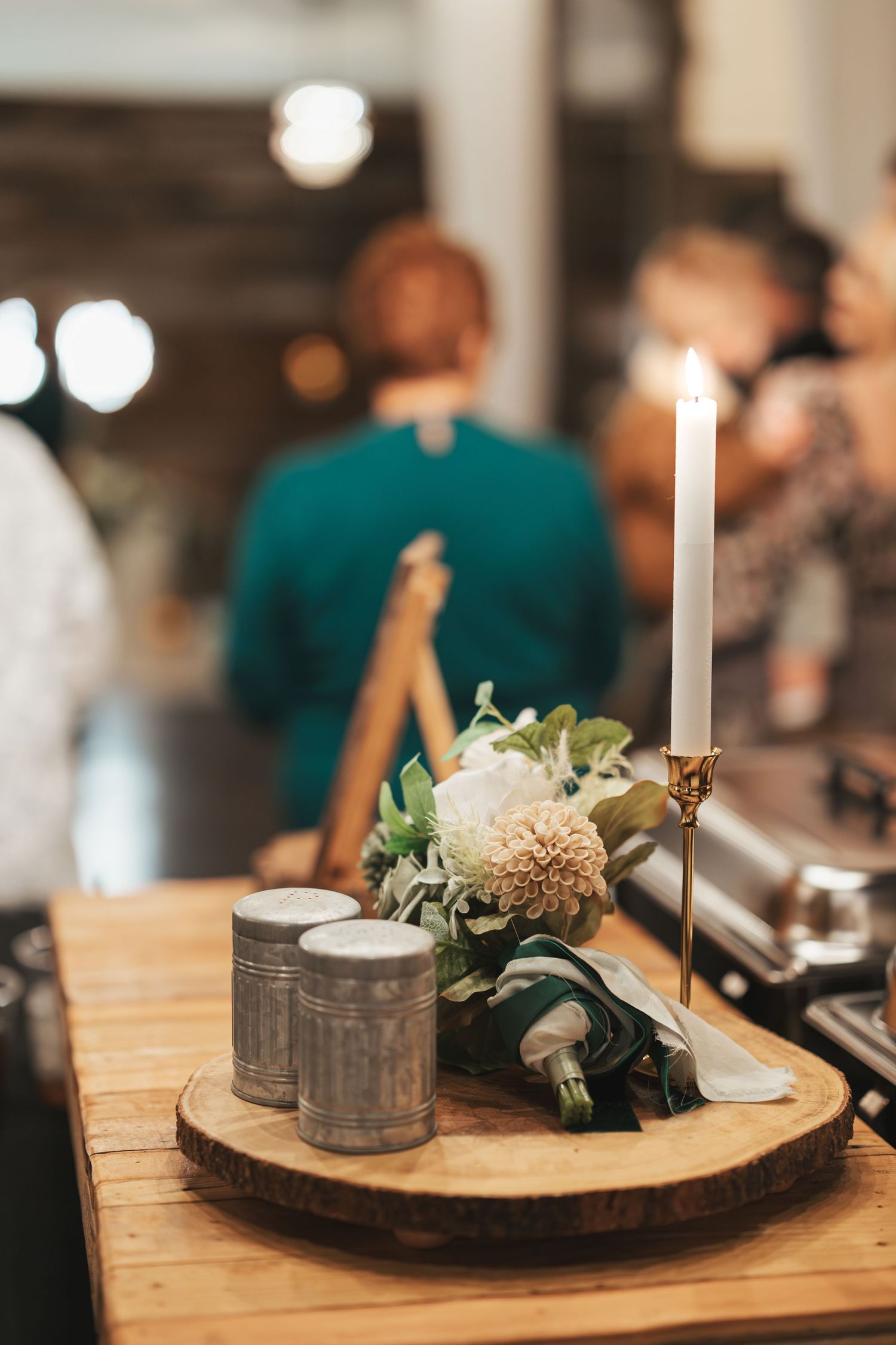 Rustic wedding centerpiece with white flowers and candle on wooden slice with decorative tins.
