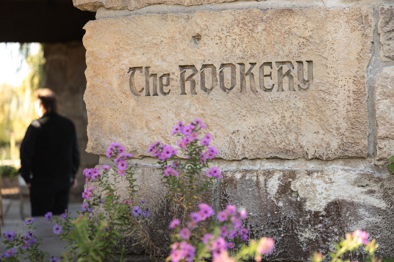 Stone sign reading 'The Rookery' with purple flowers blooming in foreground.