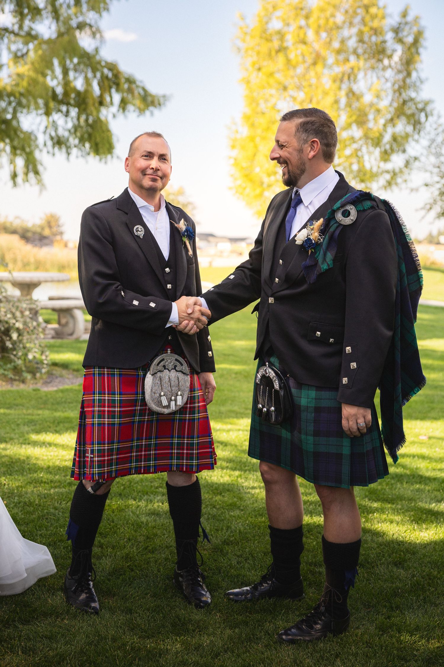 Two people in Scottish kilts with sporrans shake hands during an outdoor ceremony.