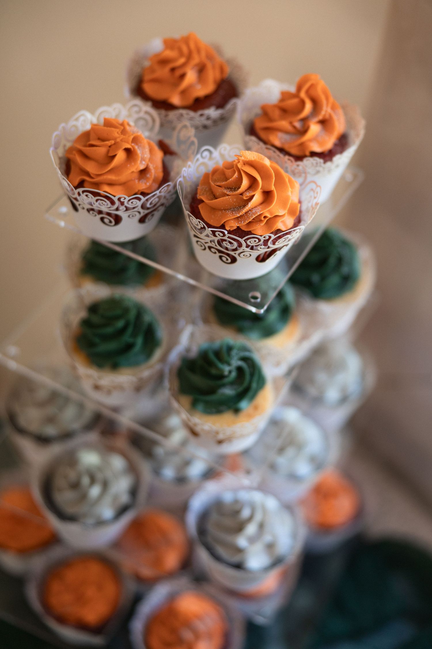 Tiered display of cupcakes with orange and teal frosting in decorative paper wrappers.