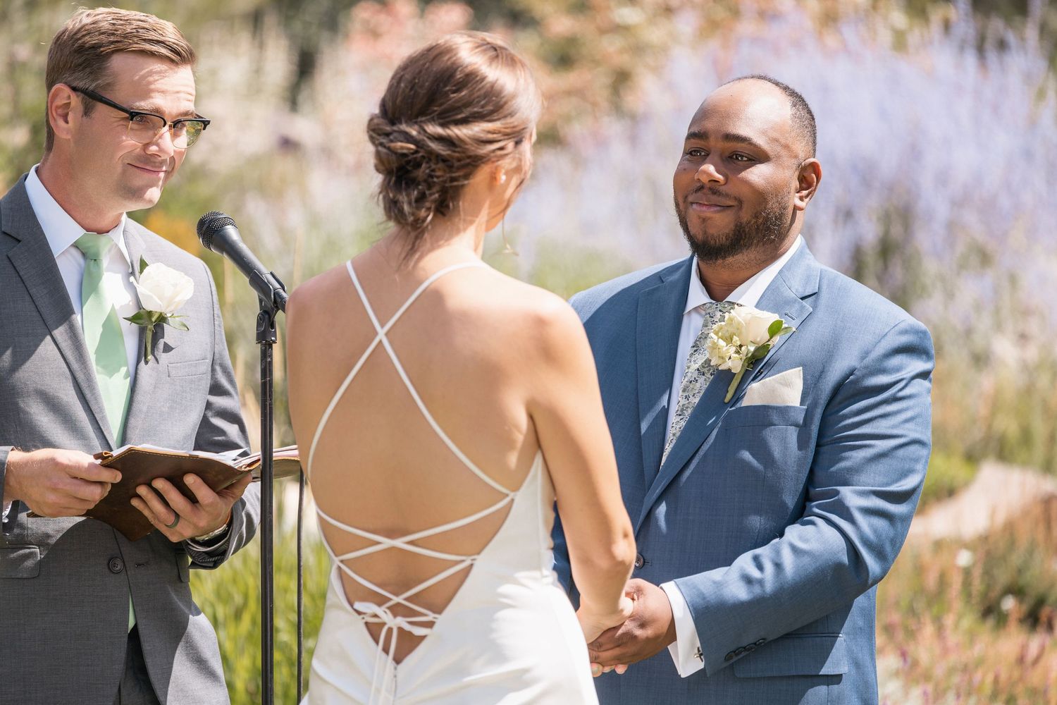 Close-up details of a wedding ceremony showing hands and rings being exchanged against a mountain backdrop.