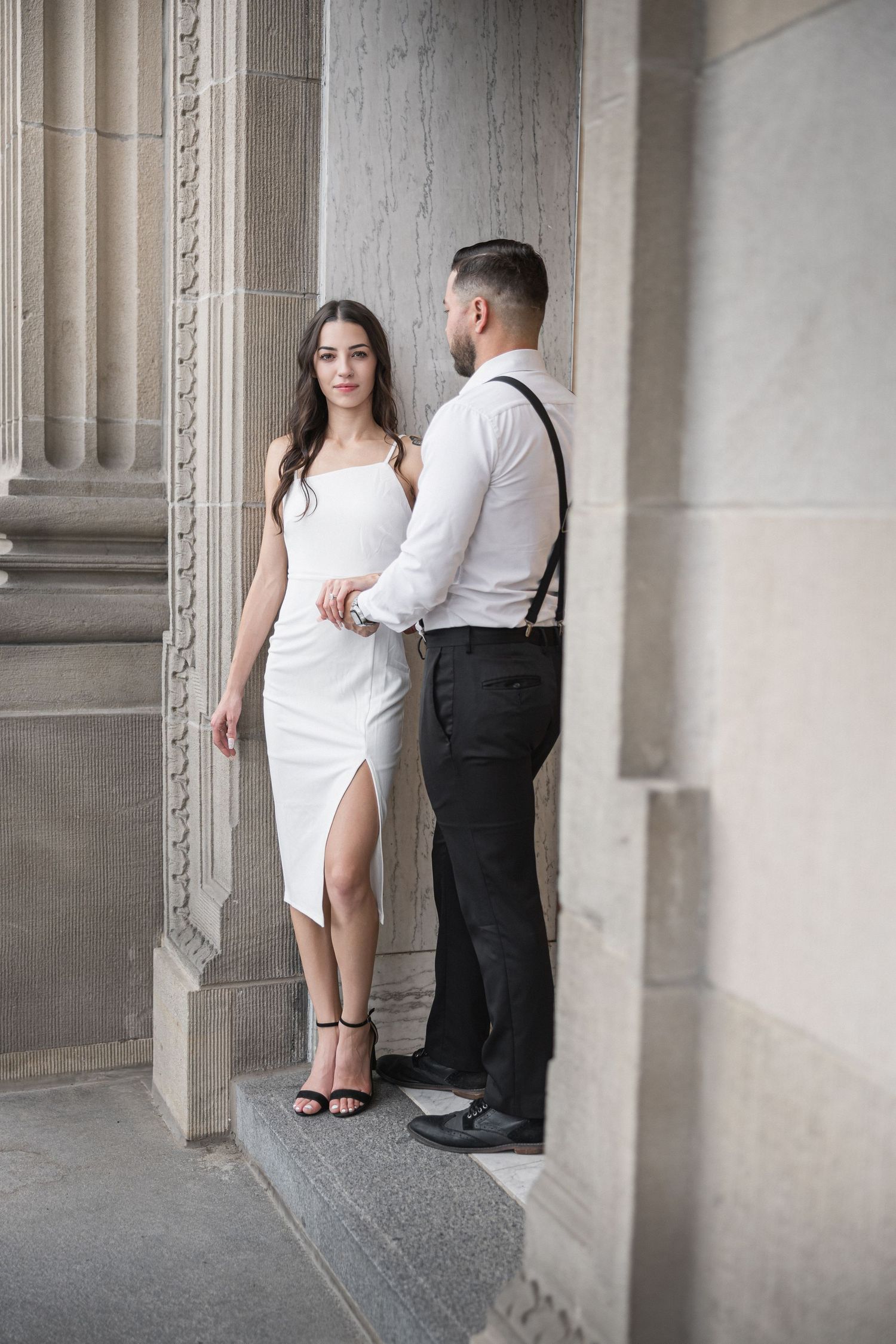 Couple in contrasting black and white outfits pose against classical stone architecture.