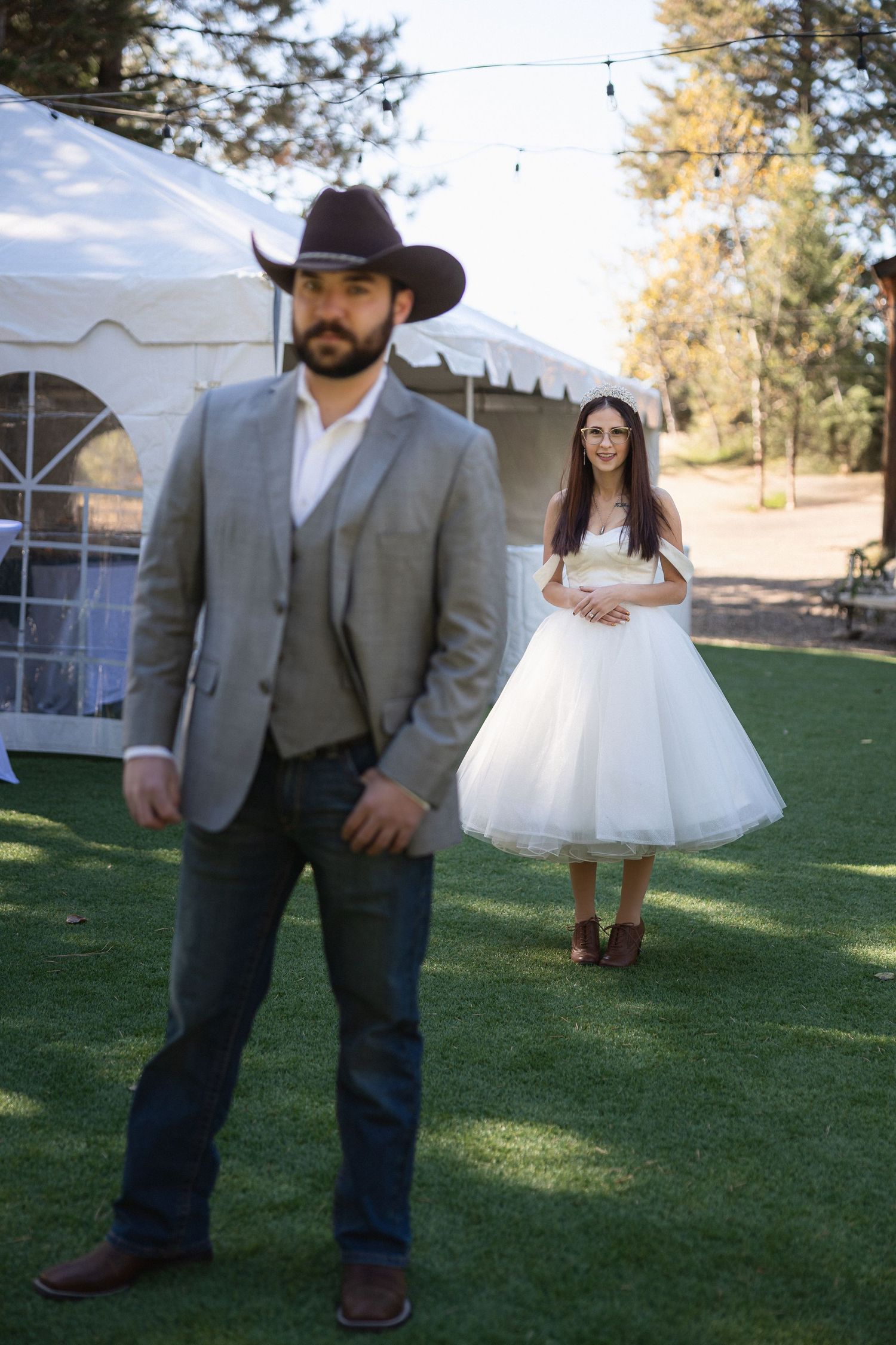 Wedding couple in western style attire posing playfully on grassy lawn.