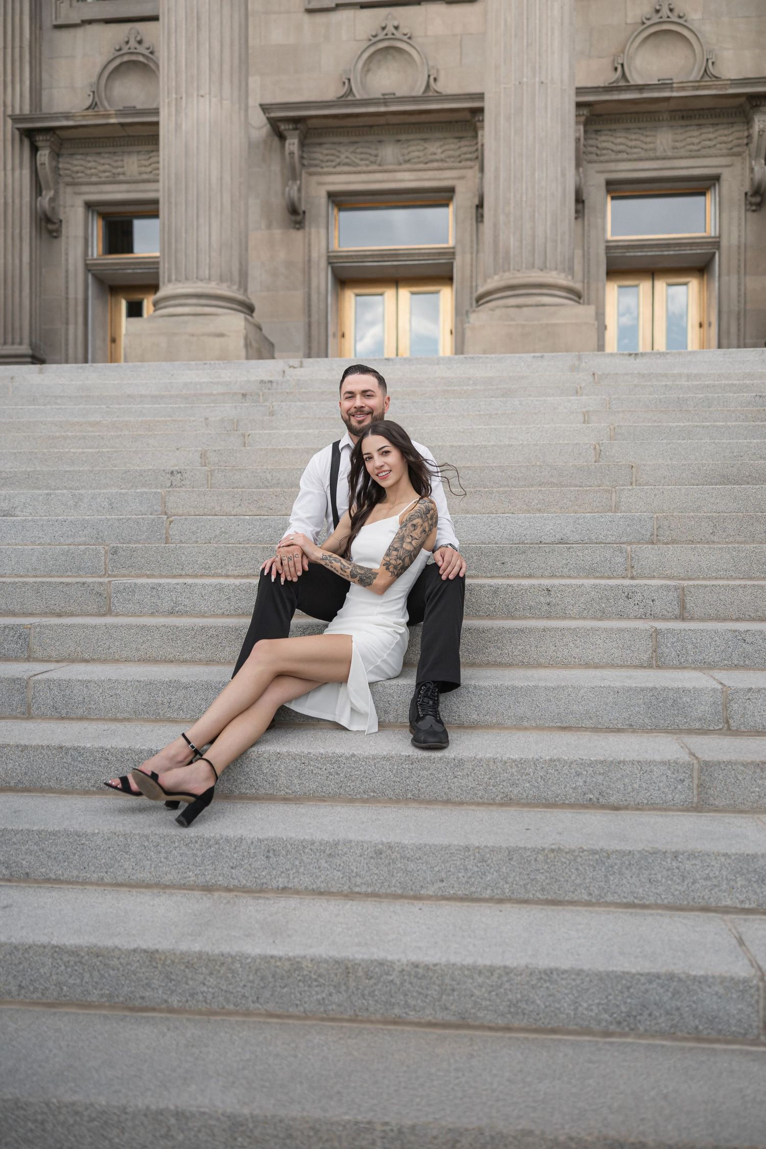 Two people relax casually on stone steps of a historic building with columns.