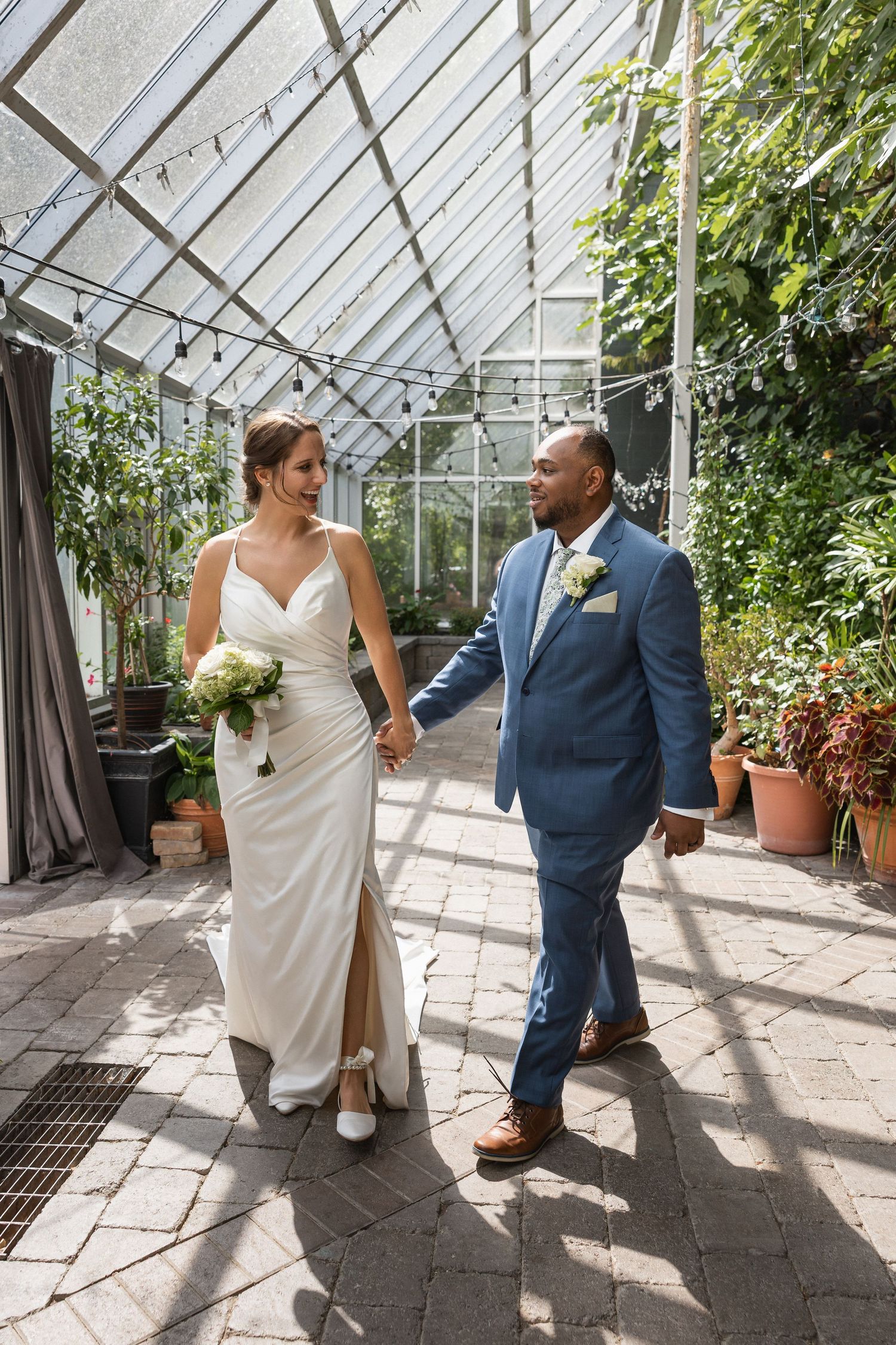 Wedding couple sharing a romantic moment in a greenhouse filled with potted plants and natural light.