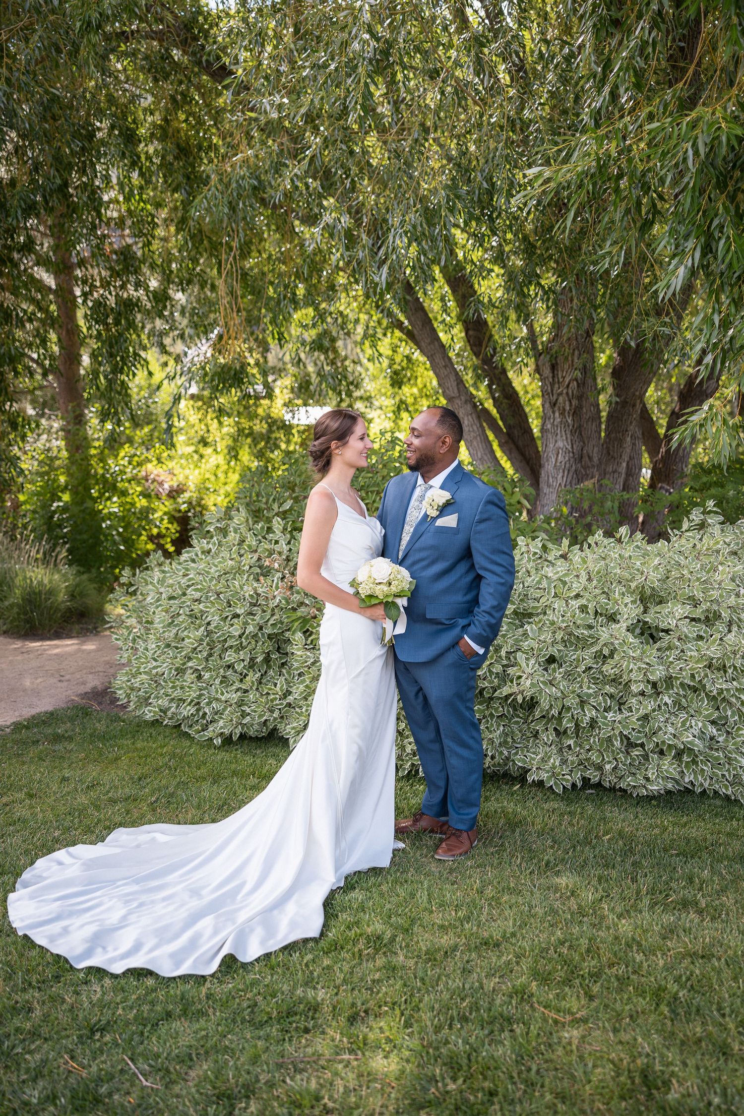 A beautiful wedding photoshoot in a garden with willow trees and white flowering bushes.