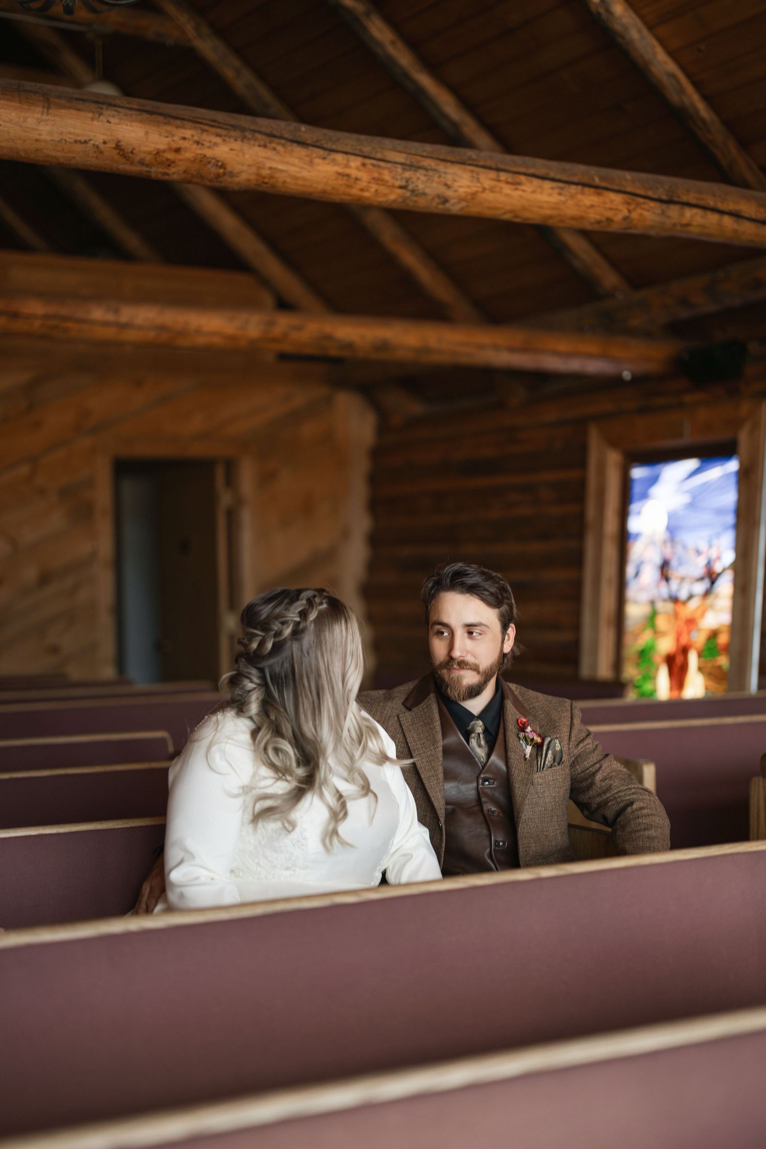 A couple sits together in vintage wooden church pews during an intimate moment.