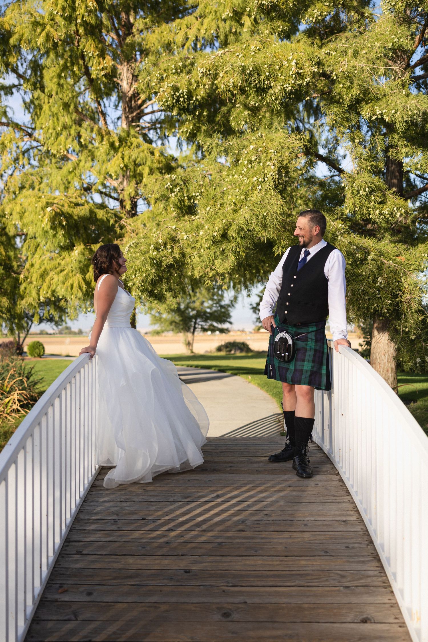 A couple stands on a white wooden bridge surrounded by yellow-leaved trees.
