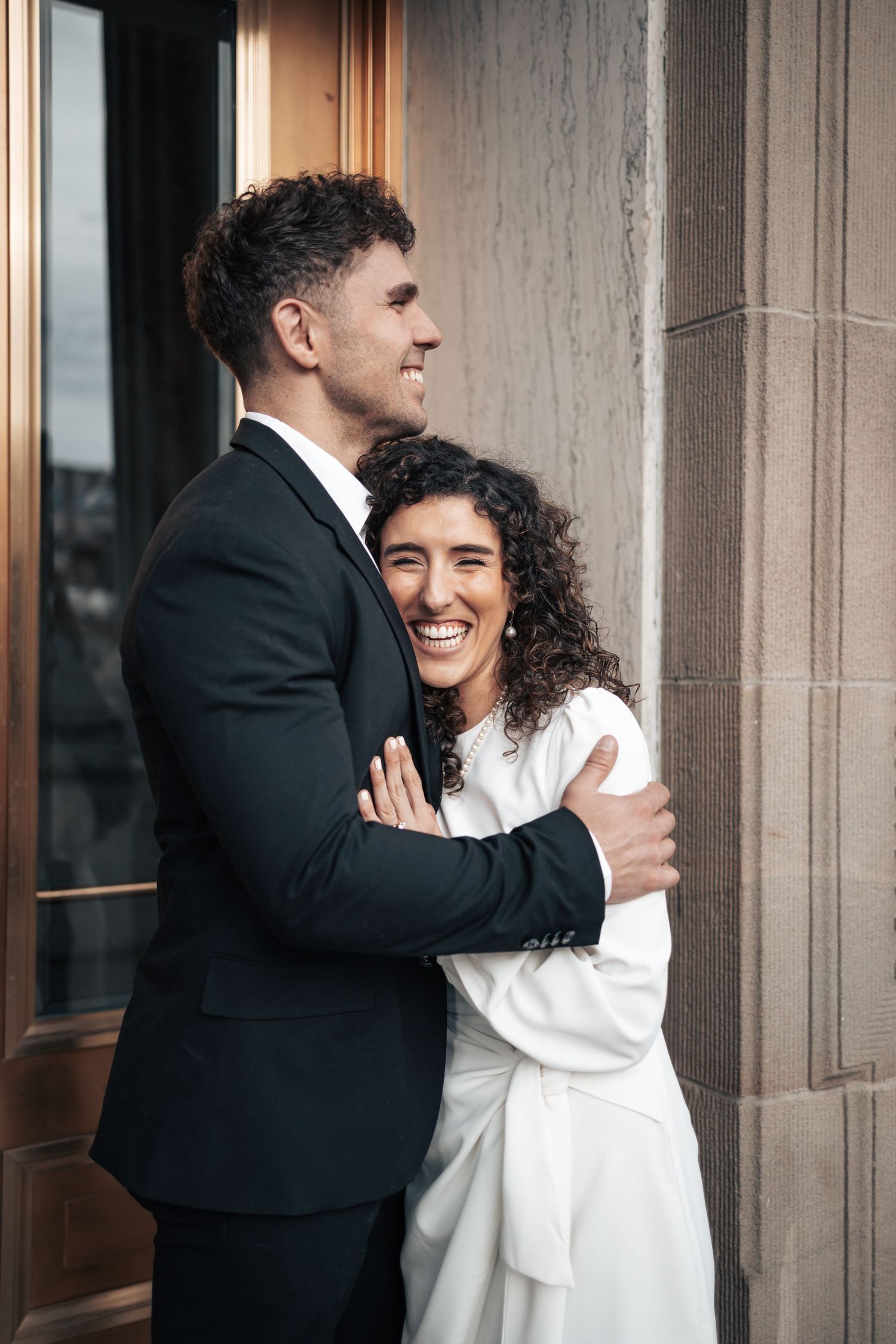 A happy couple shares a tender embrace while standing beside an elegant copper doorway.
