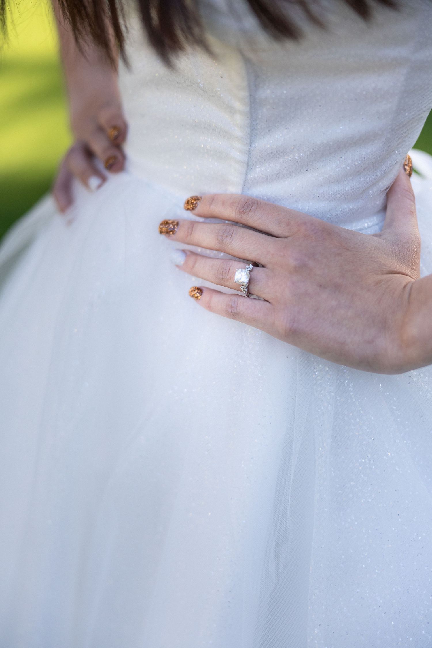 Close-up of bride's hand showing engagement ring against white tulle dress.