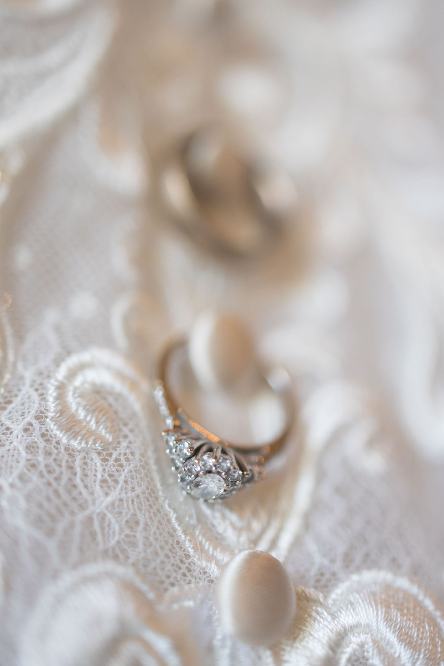 Close-up of diamond engagement ring on delicate white lace fabric with soft focus.