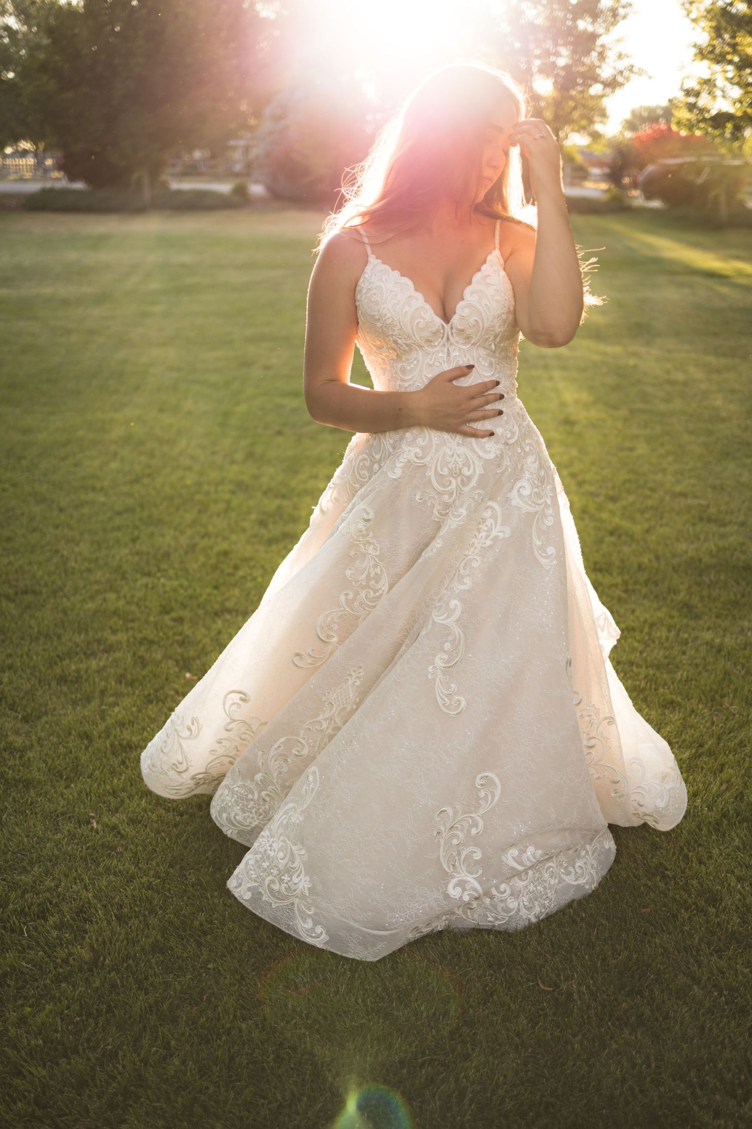 Sunlit portrait of wedding dress with intricate lace details on grassy lawn.
