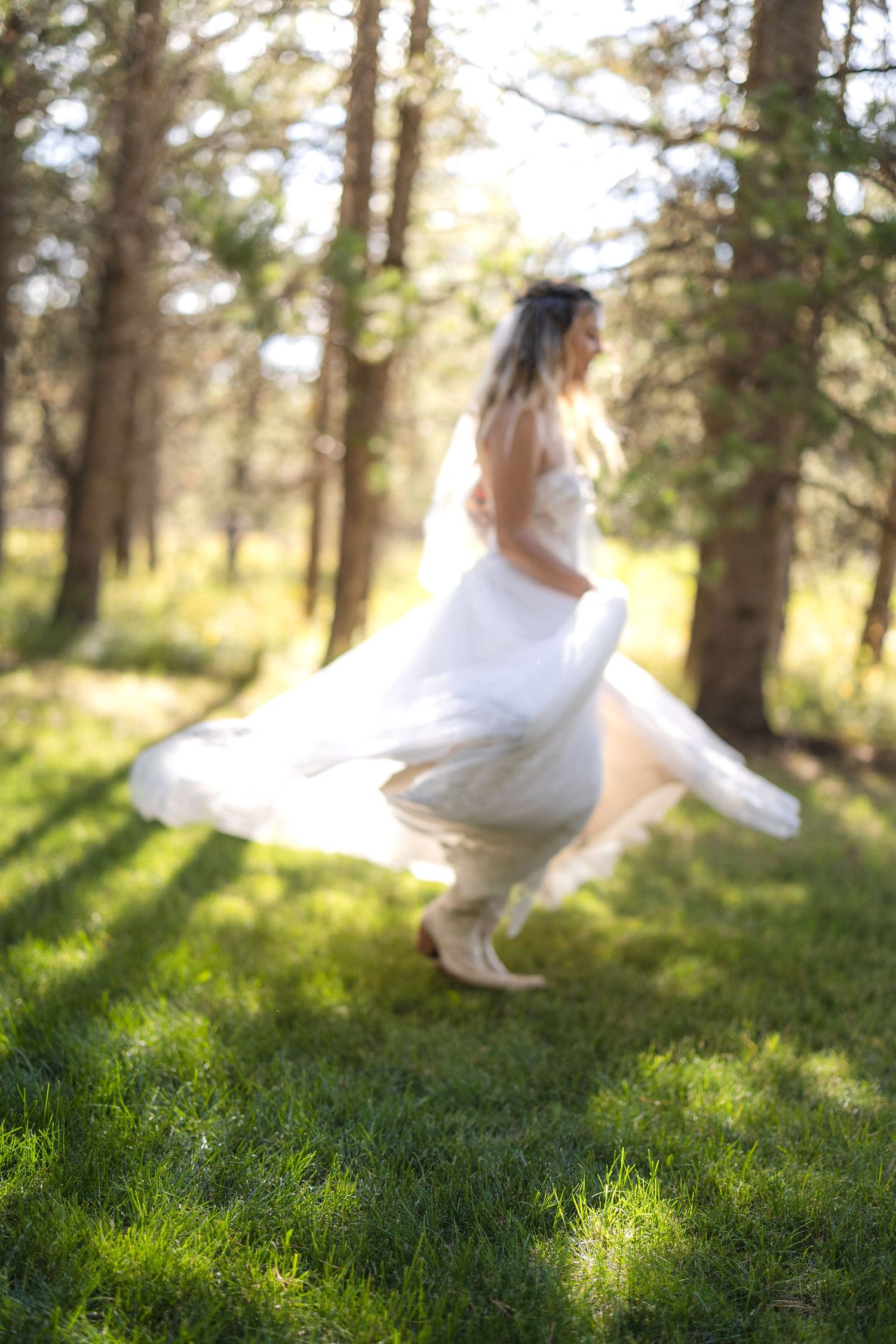Artistic motion shot of a bride dancing in her wedding dress among forest trees.
