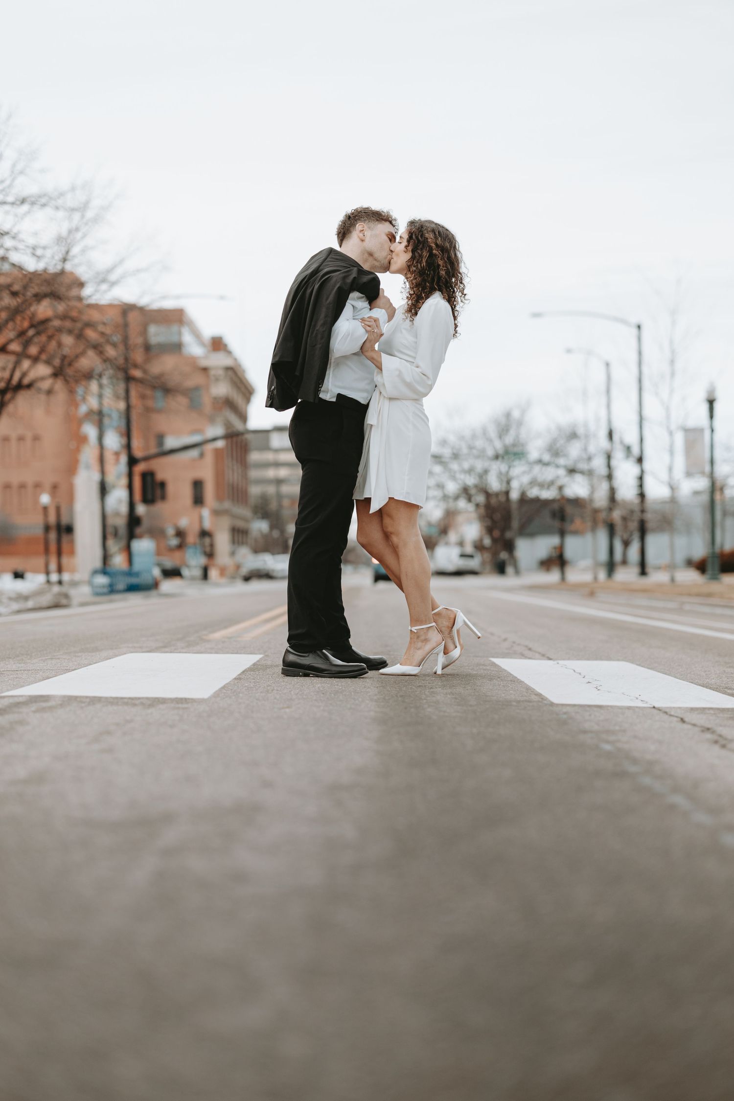 A couple in formal attire shares a romantic moment on a city crosswalk.