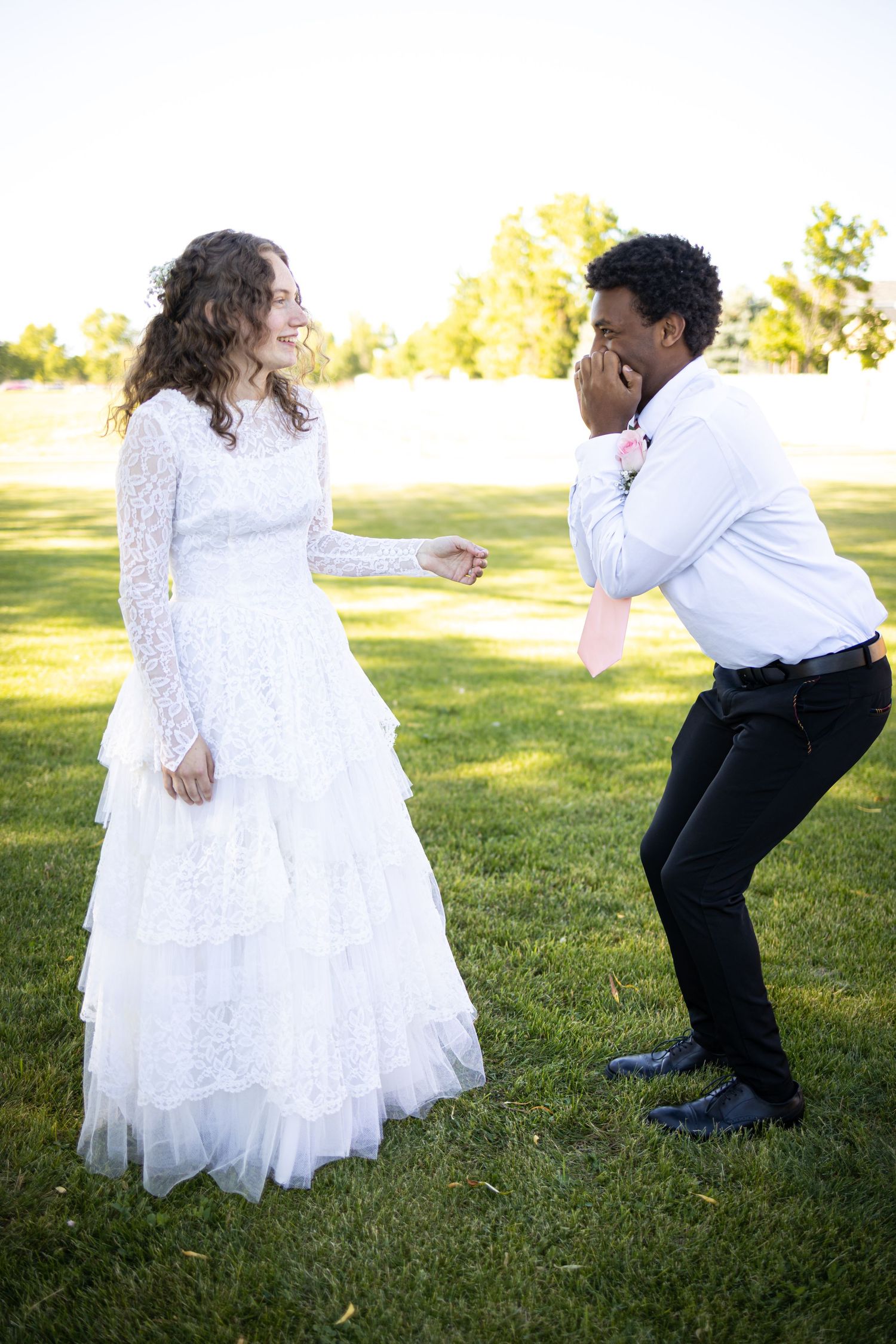 Playful wedding couple shares humorous moment on grass lawn.