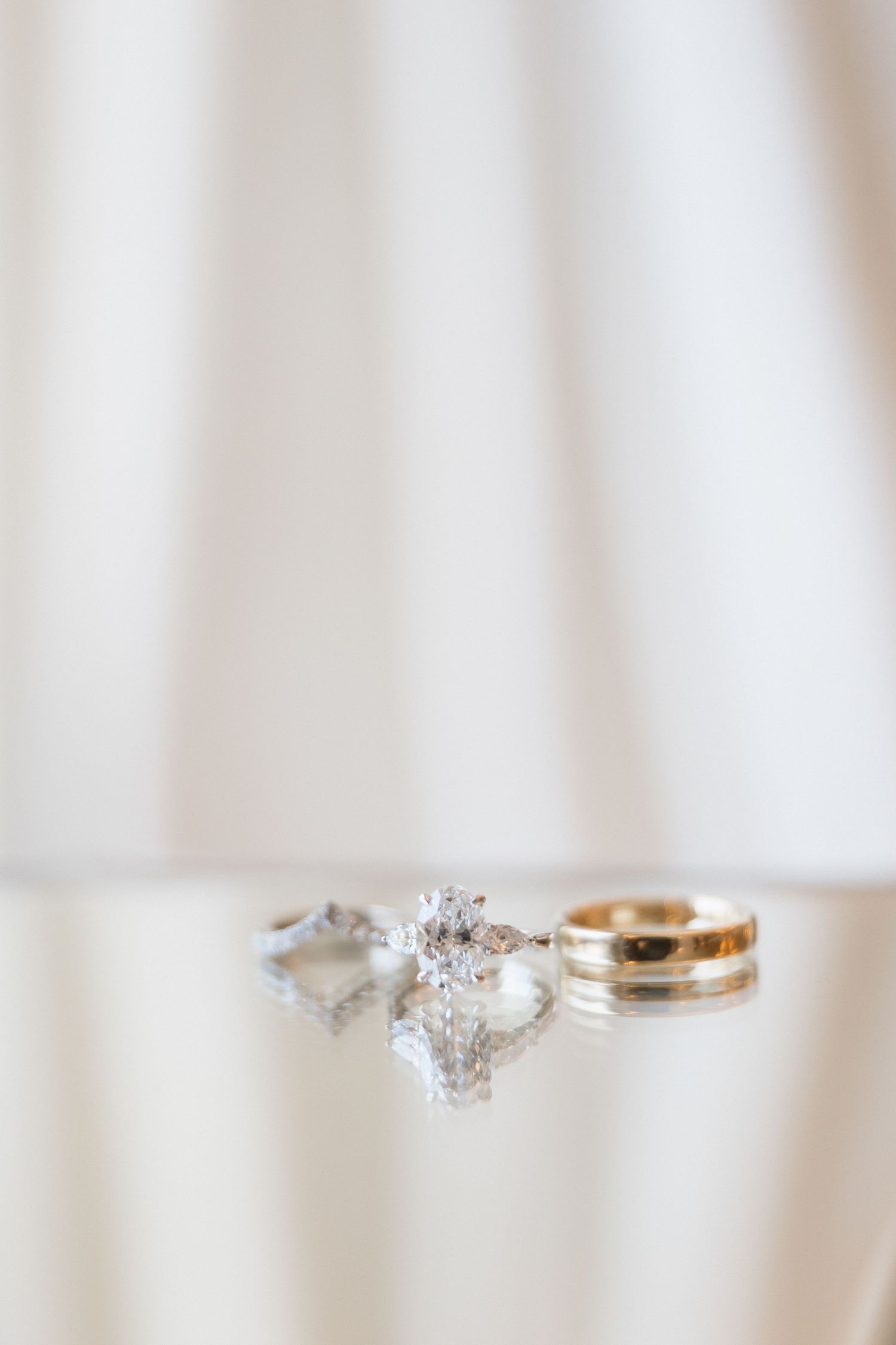Close-up of elegant diamond engagement ring and wedding bands on white background.