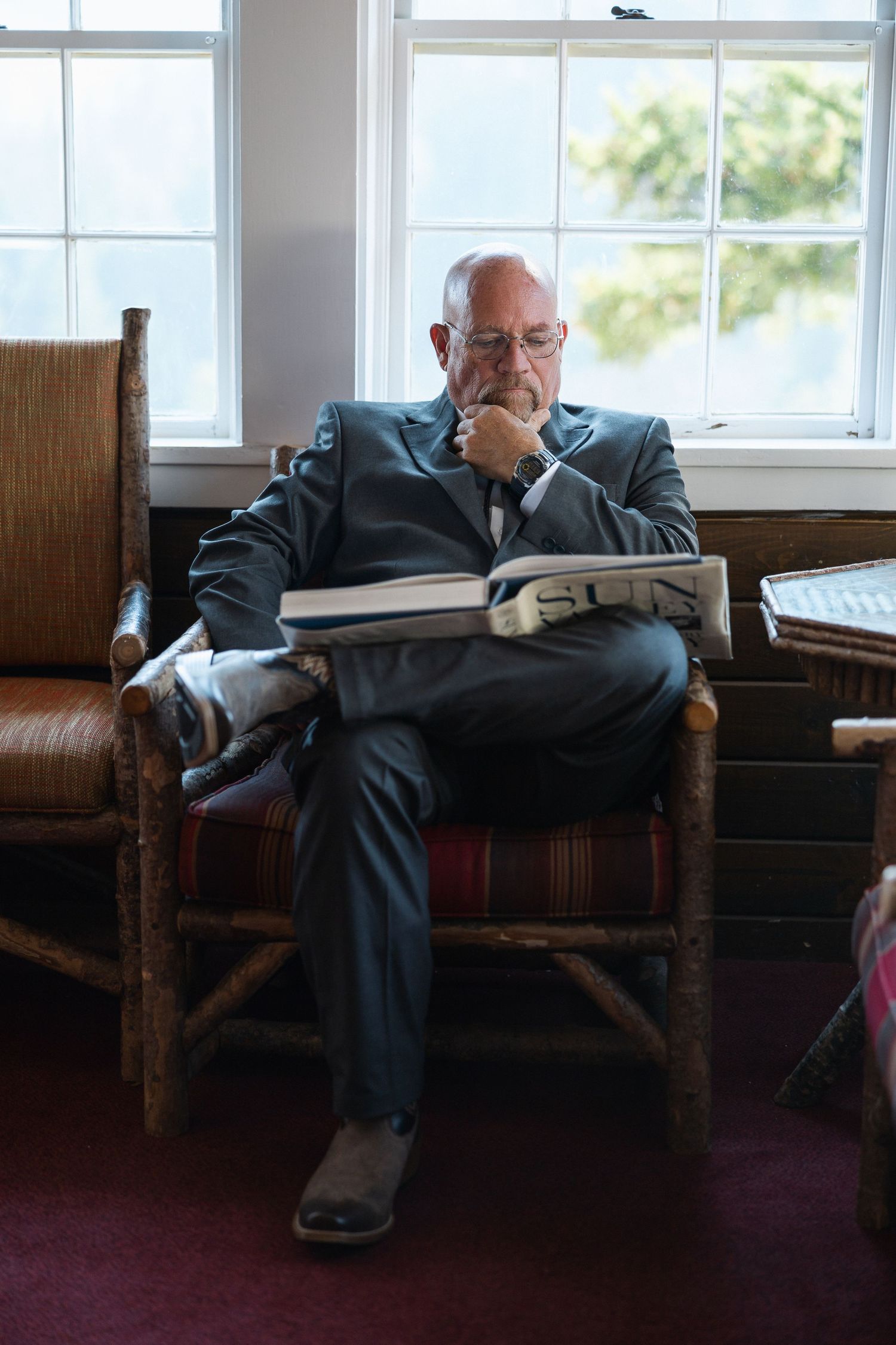 Person lounging on a wooden bench near windows in a waiting area.