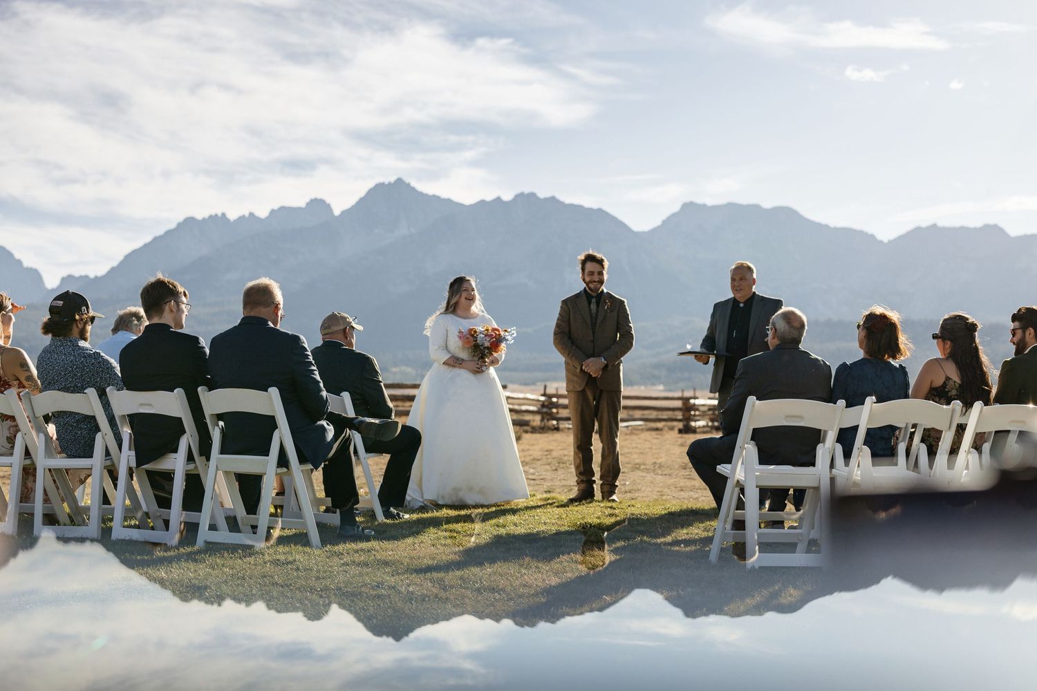 Guests seated in white chairs at an outdoor wedding ceremony with dramatic mountain peaks in the background.