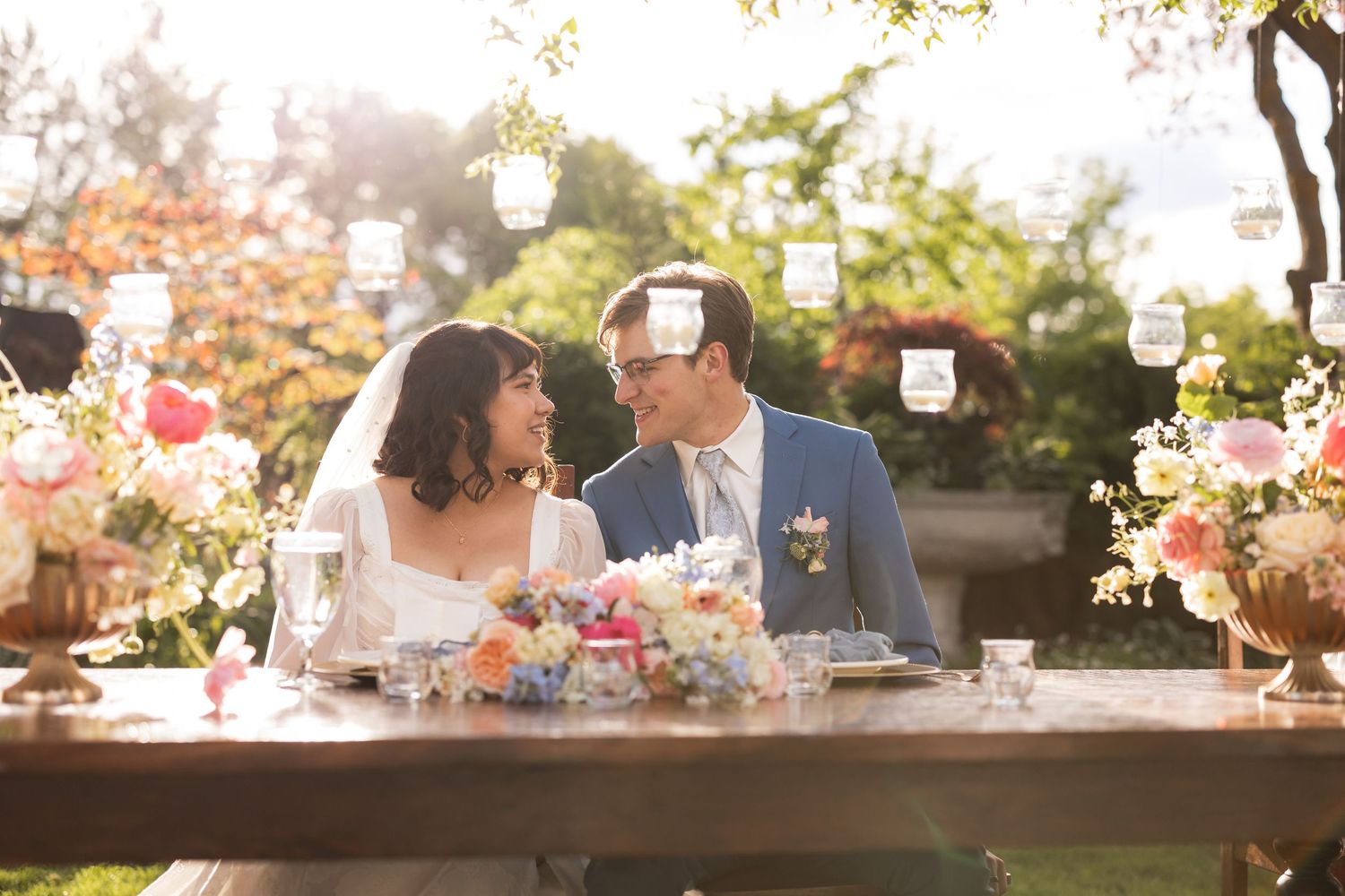 Reception tables decorated with lanterns and floral centerpieces at sunset under a canopy of trees.