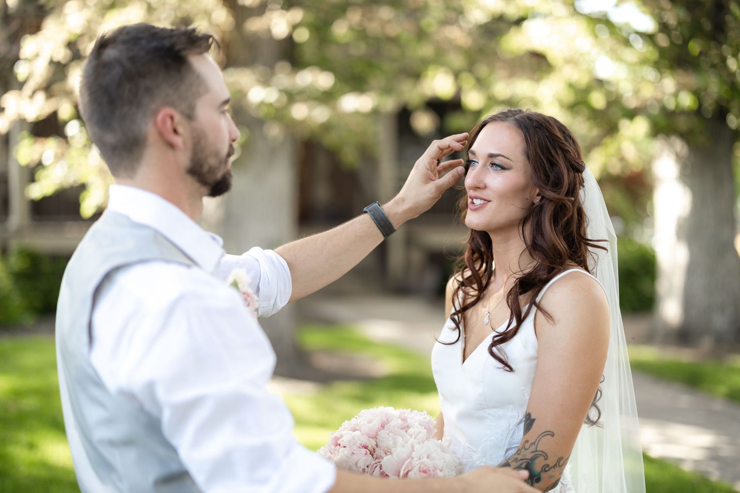 Wedding couple shares tender moment outdoors as groom gently touches bride's face.