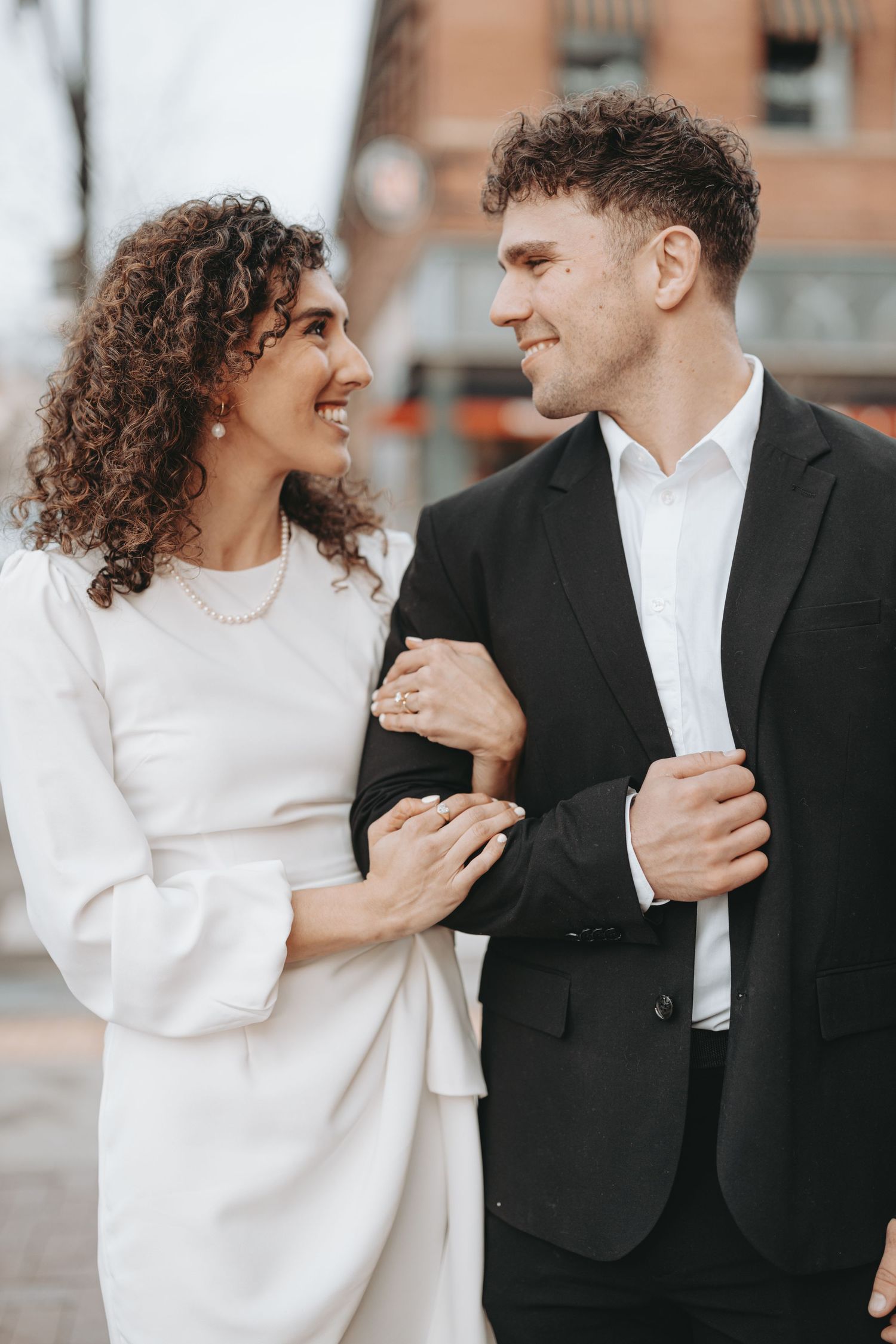 A couple in formal wear sharing a happy moment against an urban brick backdrop.