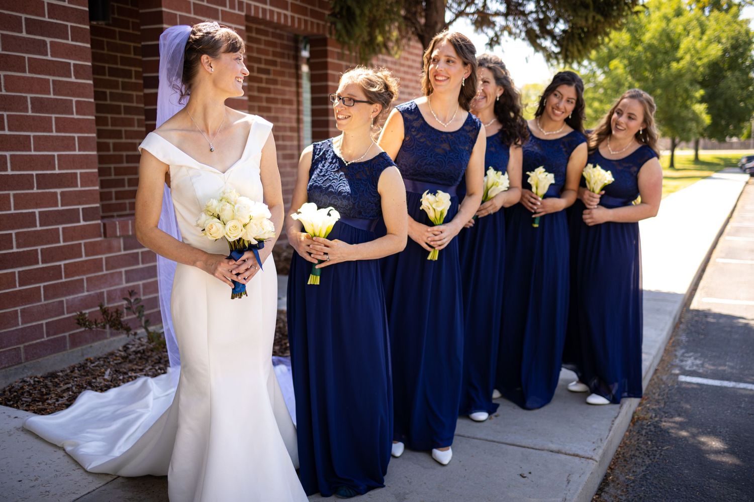 Wedding party with bridesmaids in navy blue dresses lined up against brick wall.