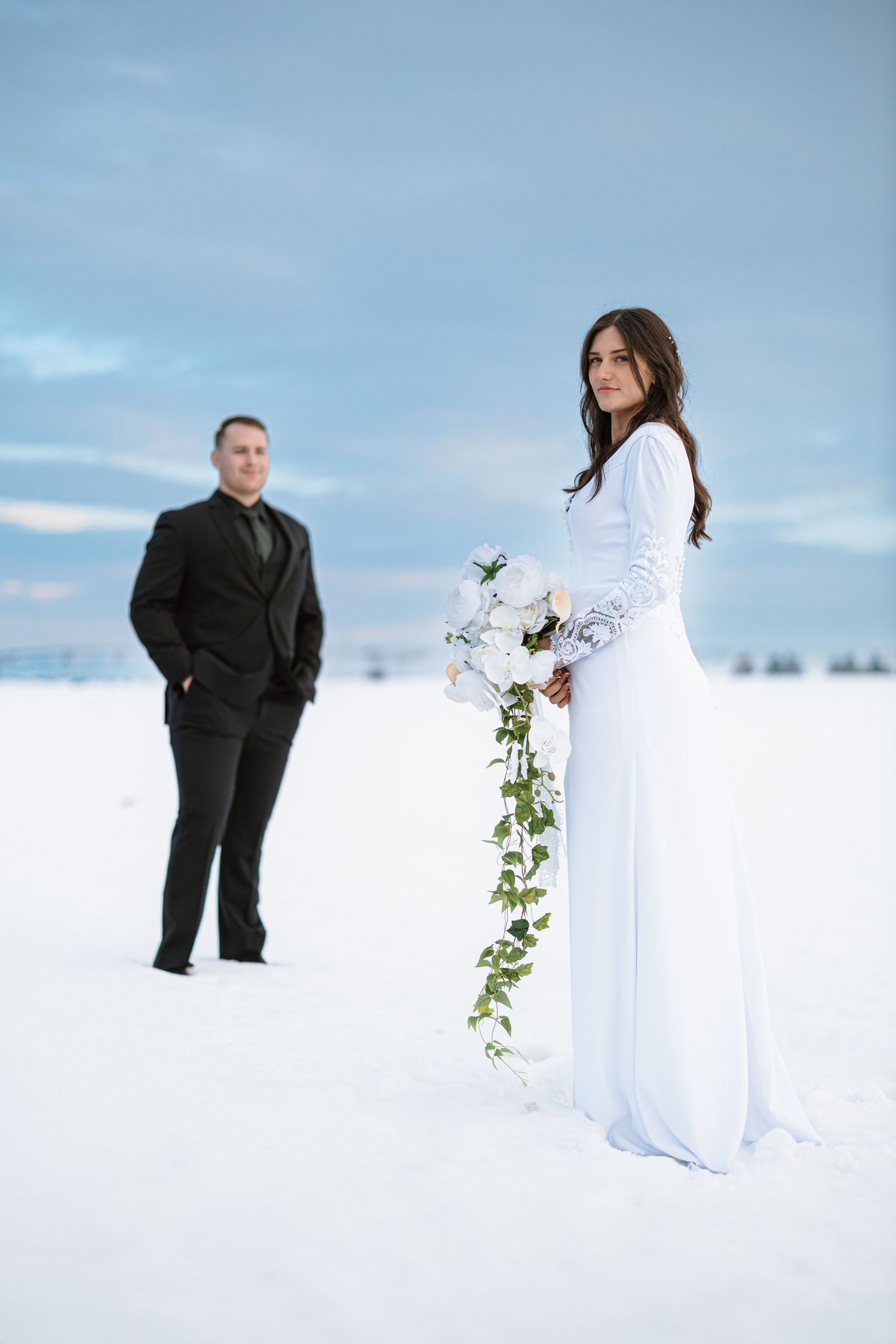 A winter wedding scene features a couple in contrasting formal wear standing in deep snow.