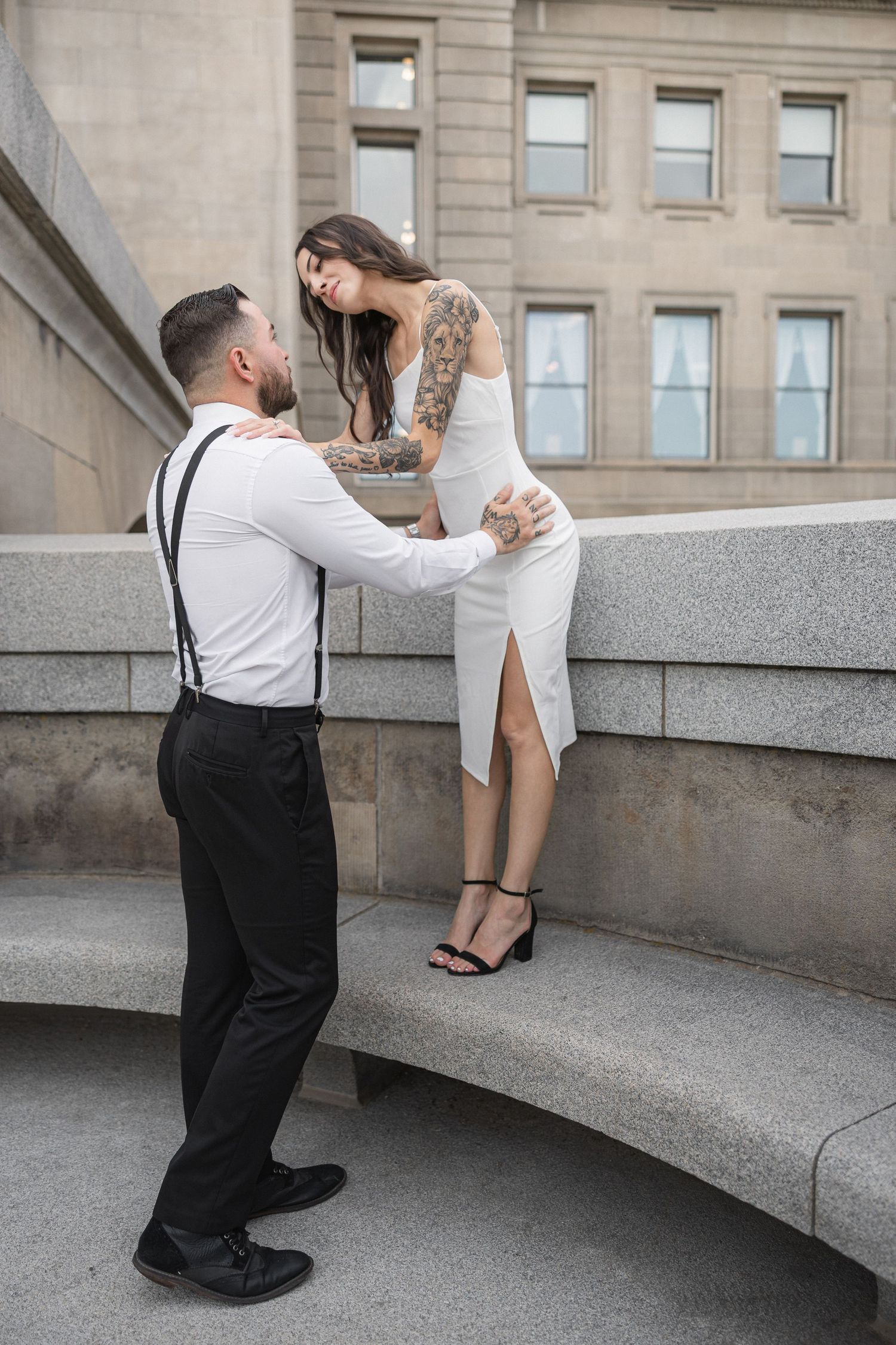 Tender engagement moment captured on curved stone steps of an elegant architectural setting.