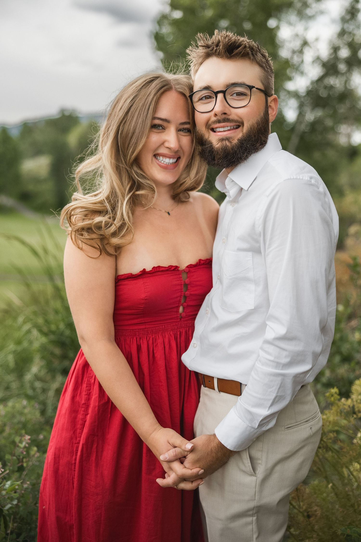 A couple in a red dress and white shirt pose together outdoors in a romantic portrait session.