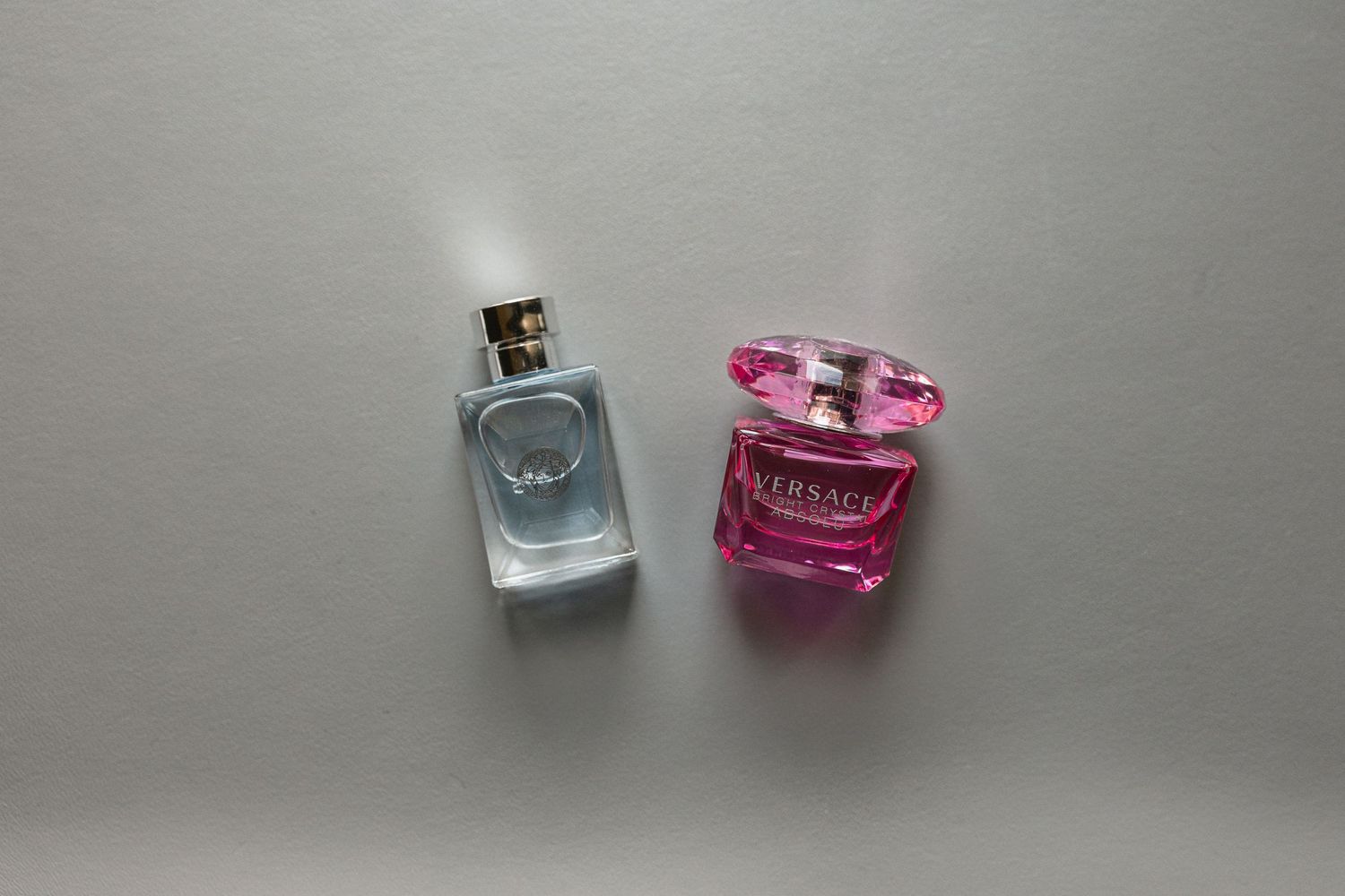 Two perfume bottles, one blue and one pink, arranged on gray background.