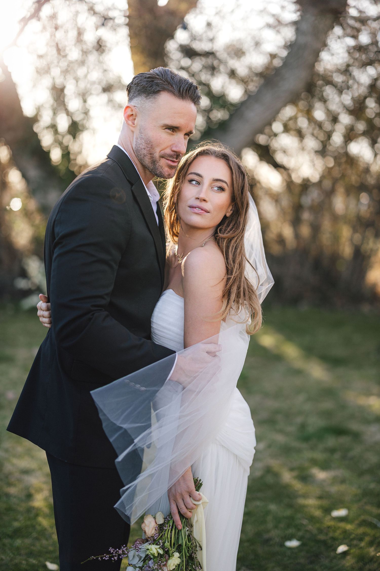 Romantic sunset wedding portraits with flowing veil in a natural outdoor setting.