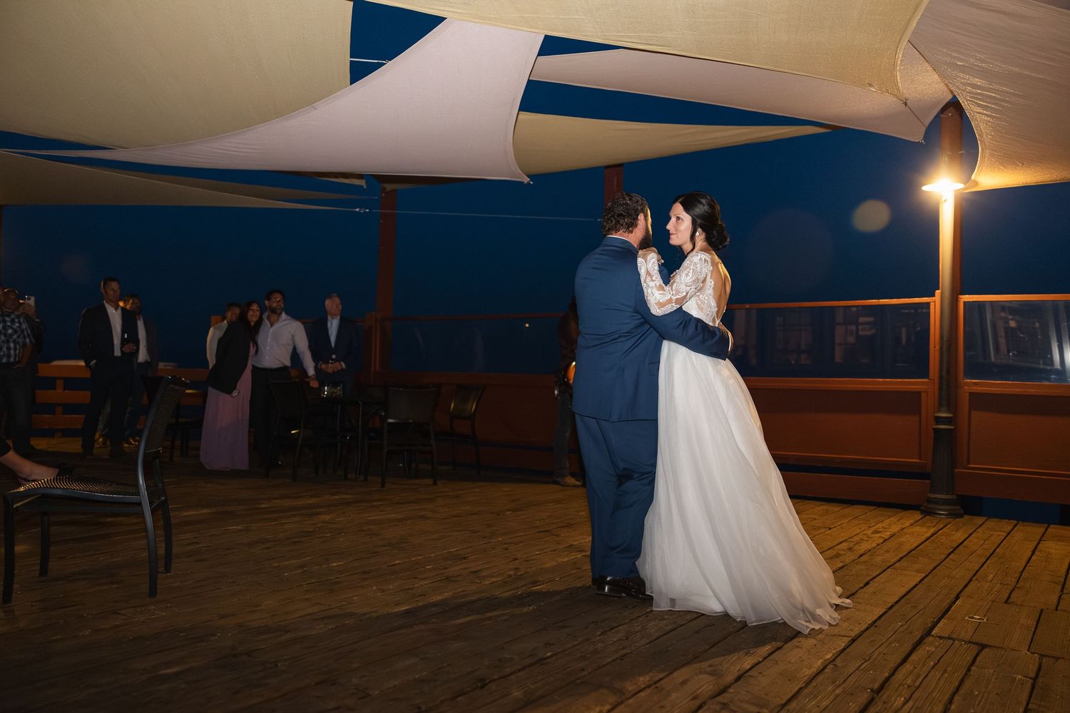 Wedding couple dancing under illuminated canopy sails at evening reception.