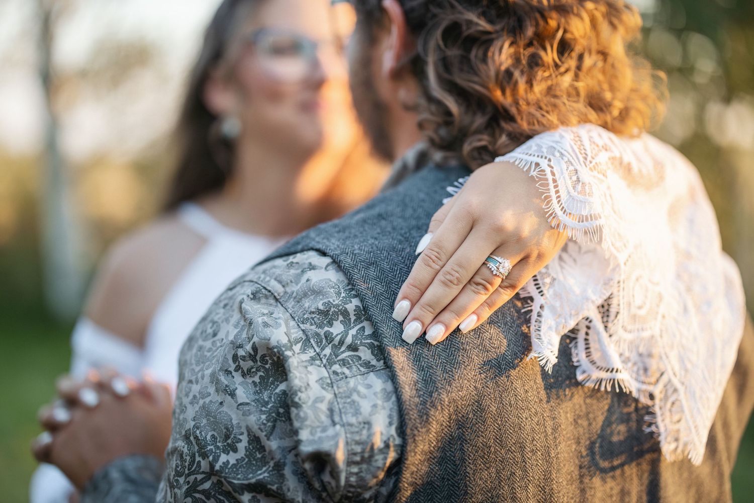 Sunlit wedding portrait showing close-up details of lace dress and boutonniere at sunset.