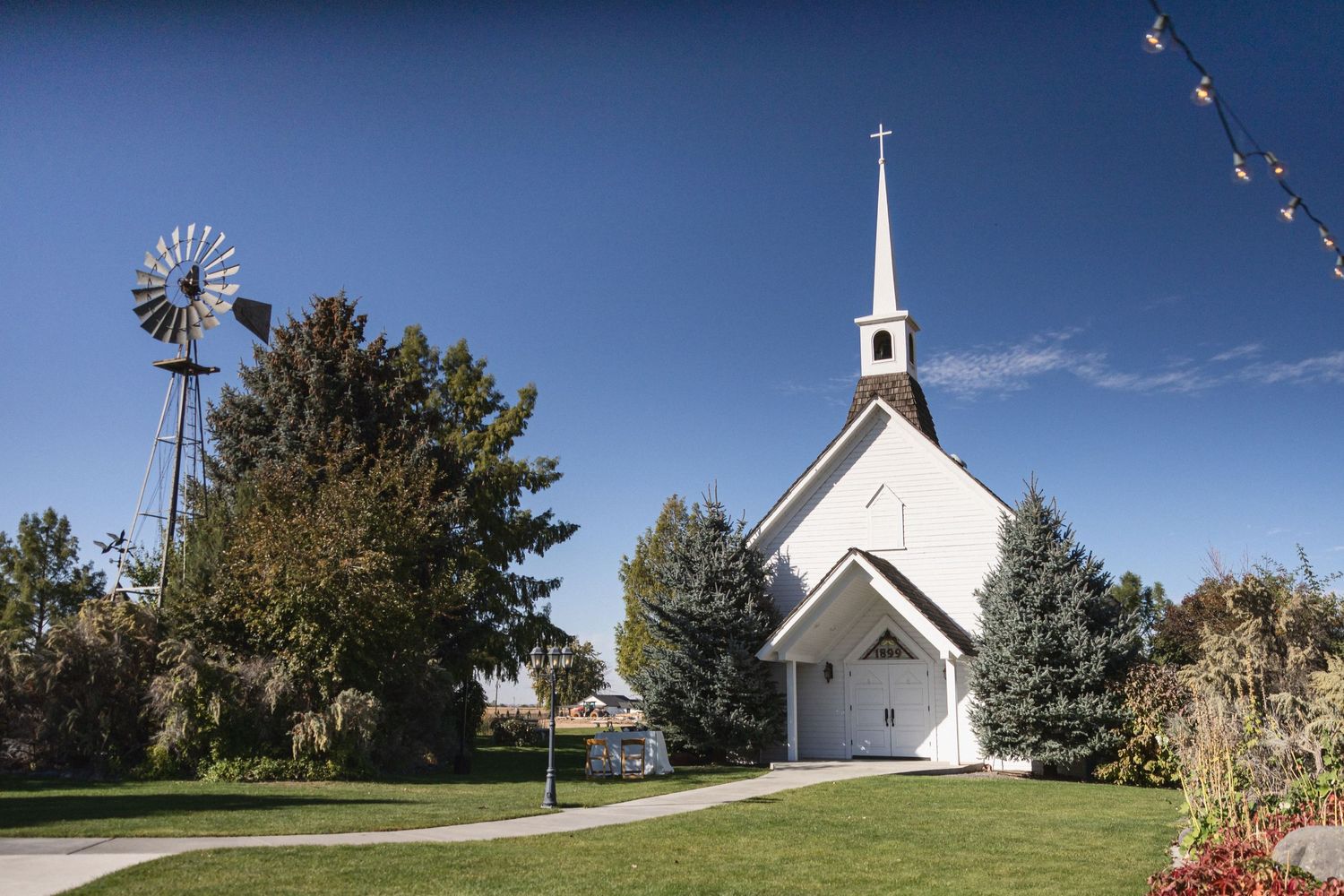 A charming white country church with a windmill against a bright blue sky.