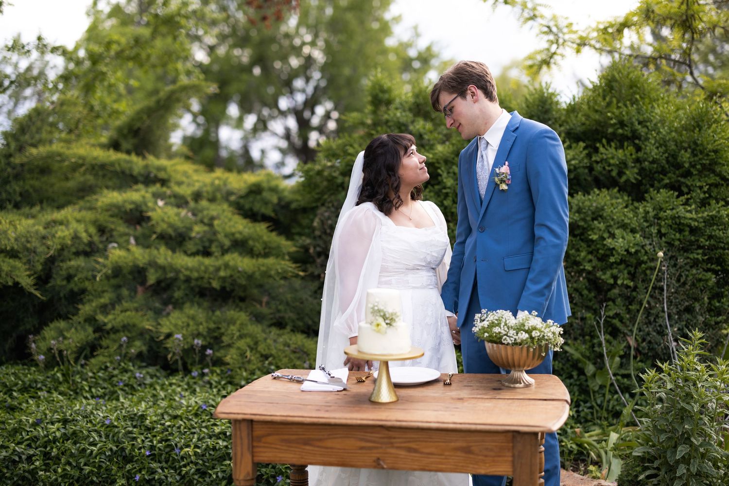 Couple stands at rustic wooden table during outdoor wedding celebration.