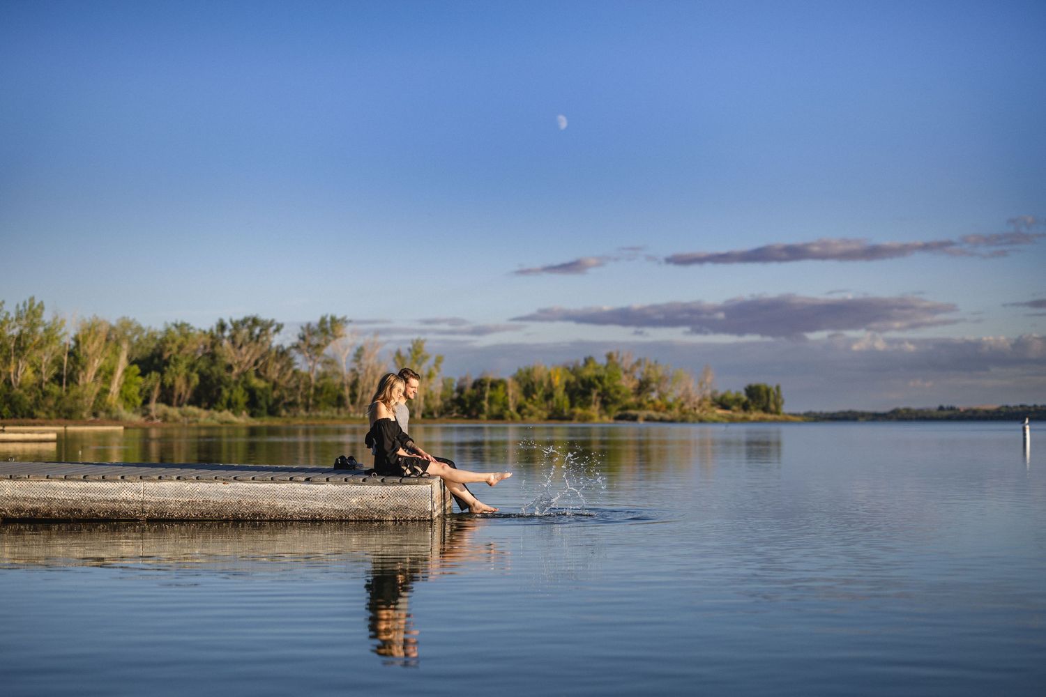 Person relaxing on wooden dock by serene lake during golden hour.
