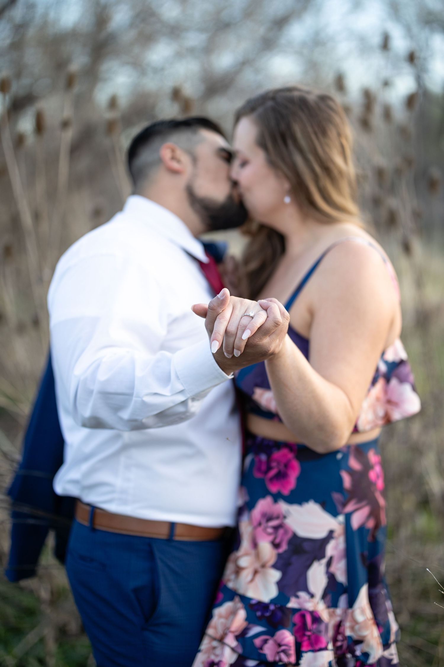 A romantic couple shares a tender kiss while holding hands during their outdoor photoshoot.