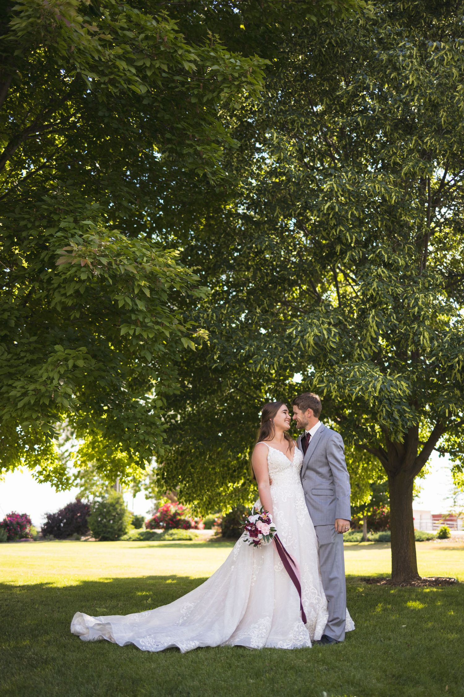Romantic wedding portrait of couple standing under large tree in afternoon light.