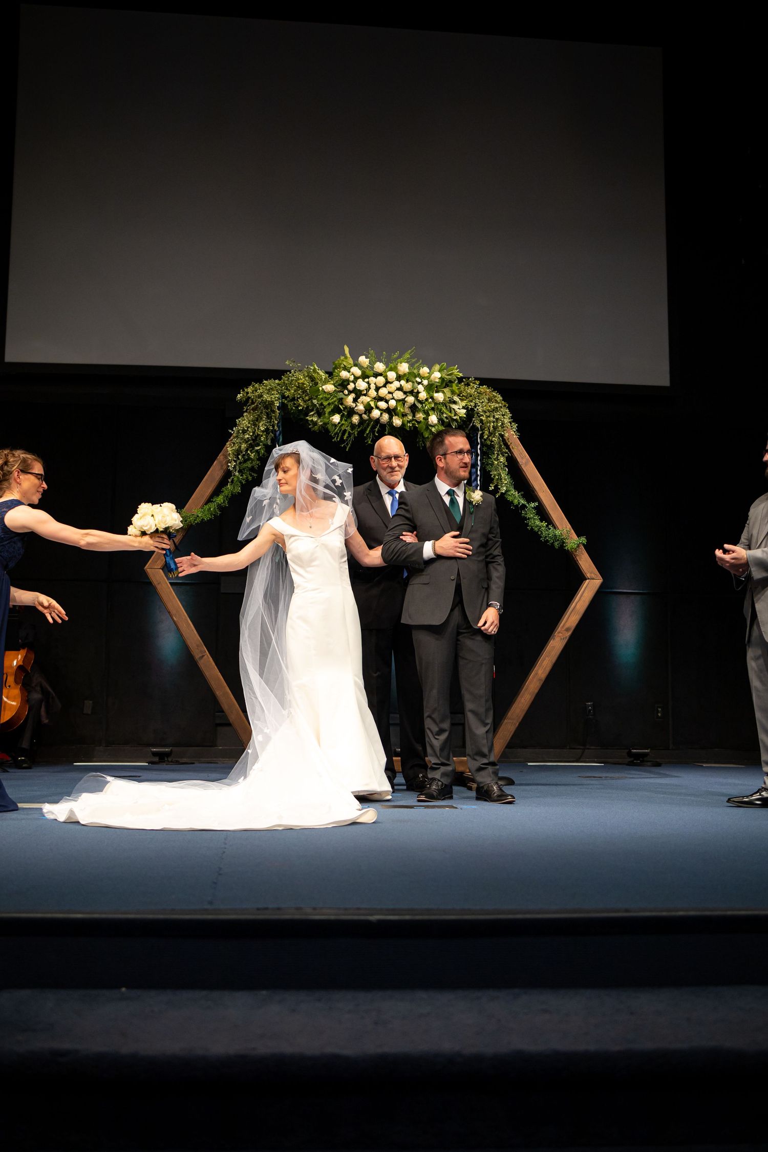 Wedding party gathered beneath a hexagonal arch with white floral arrangements.