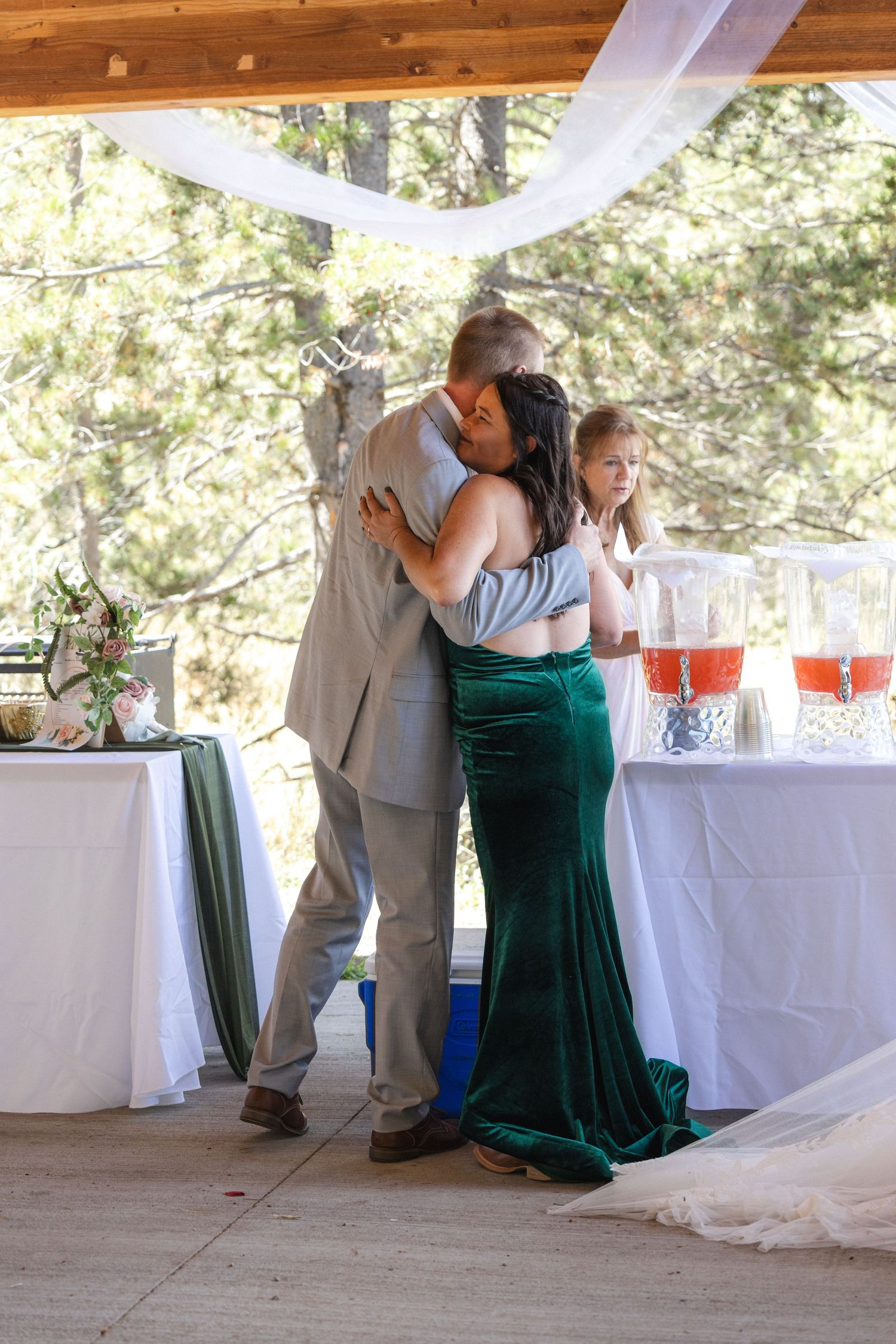Wedding celebration with elegant couple embracing in a decorated pavilion with green velvet dress and refreshments.